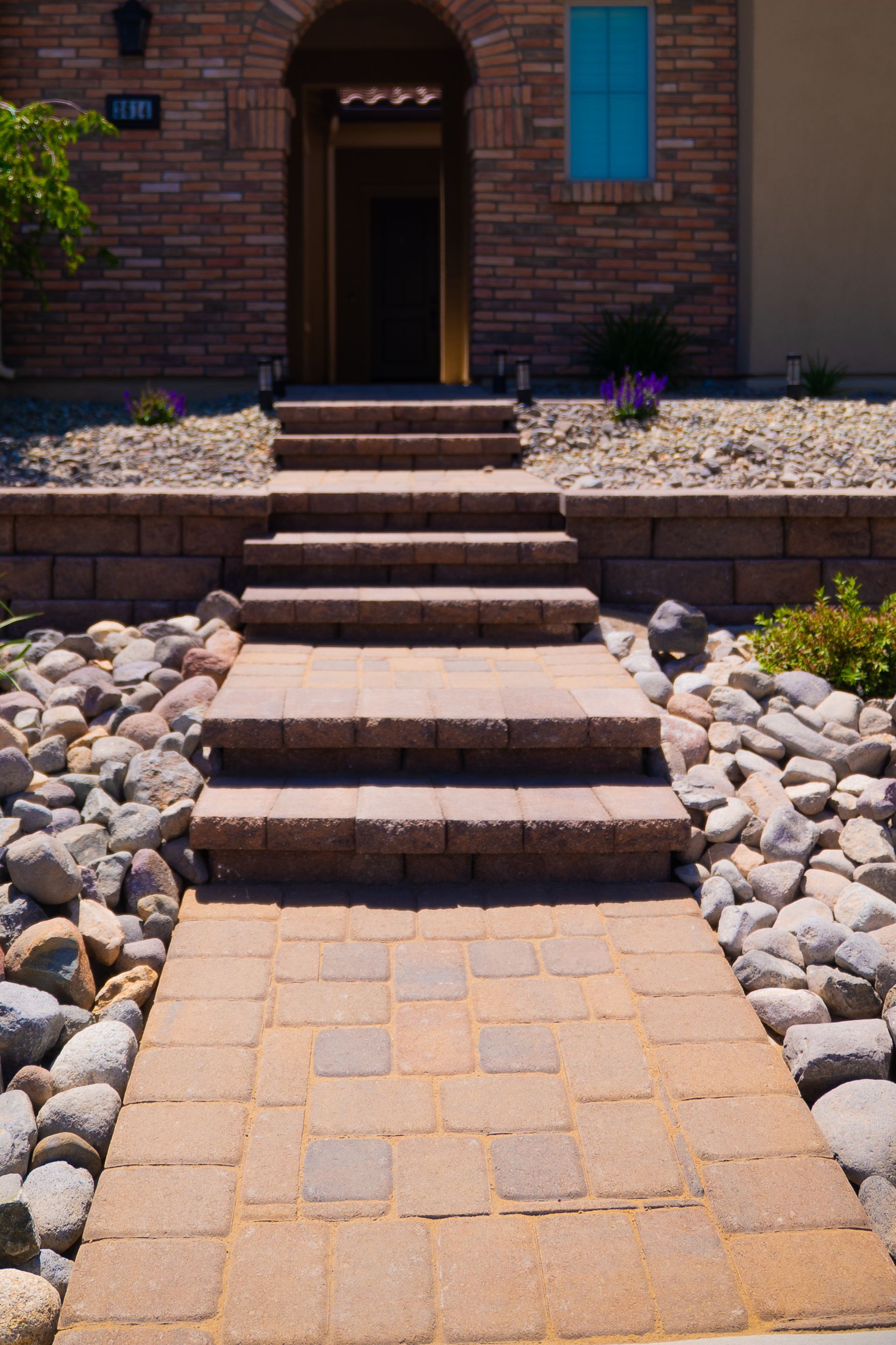 Stone pathway and steps leading to a brick home's arched entrance. Brown and tan tones.