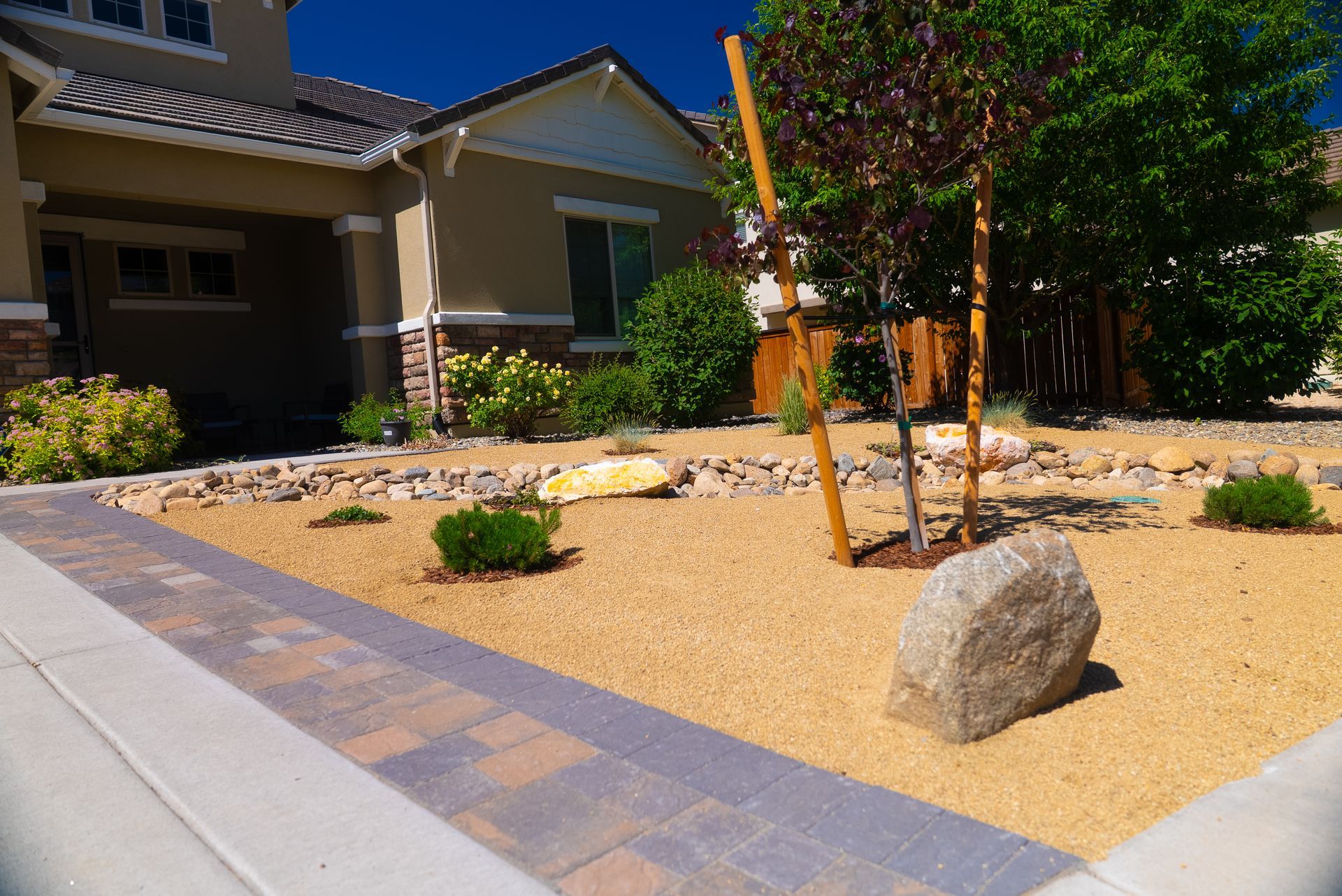 Front yard landscaping with tan gravel, rocks, and small plants next to a house with beige siding.