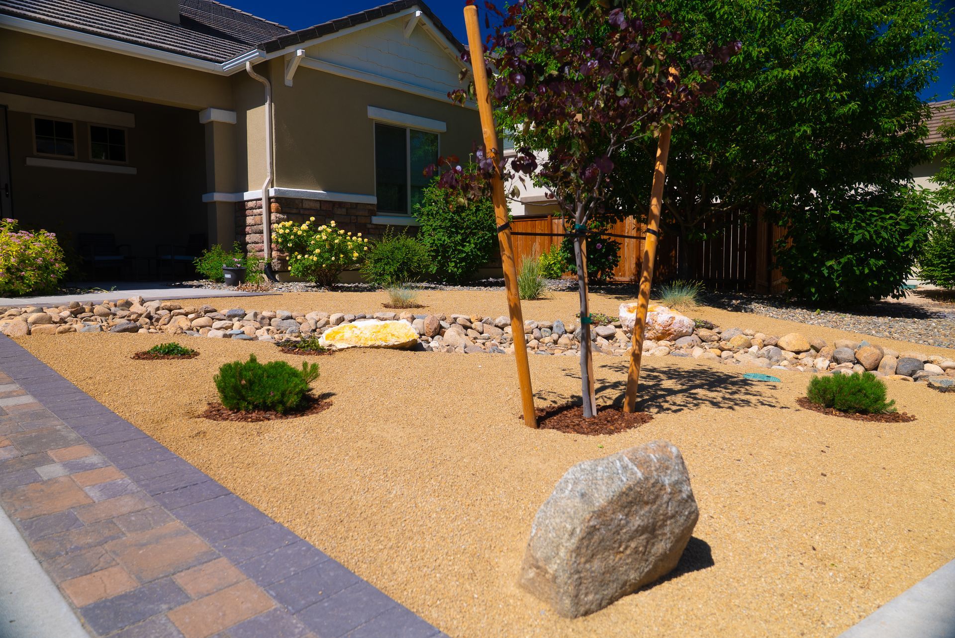 Landscaped front yard with small tree and large rocks in tan gravel. House in background.
