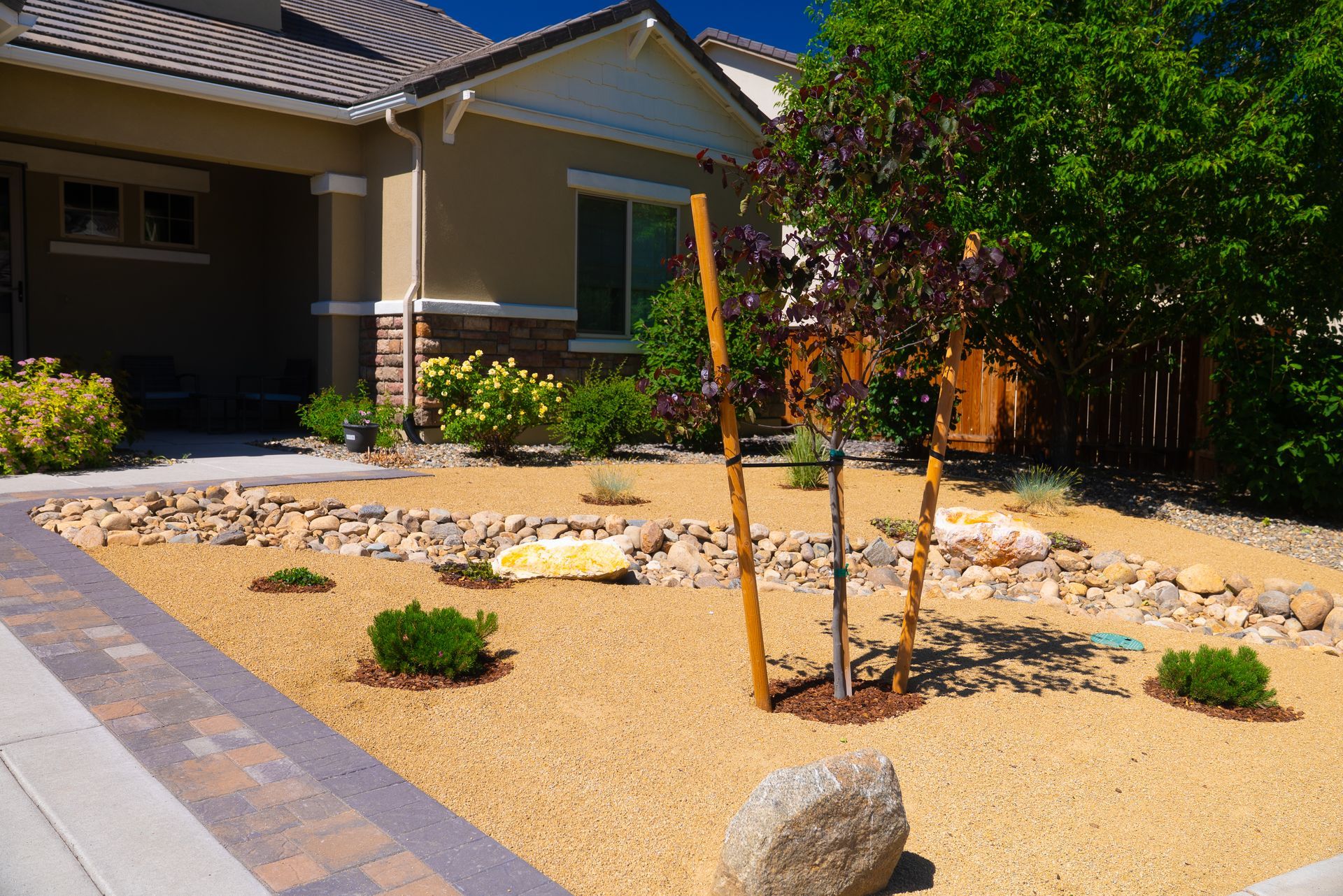 Front yard landscaping with tan gravel, rocks, and small plants in front of a beige house.