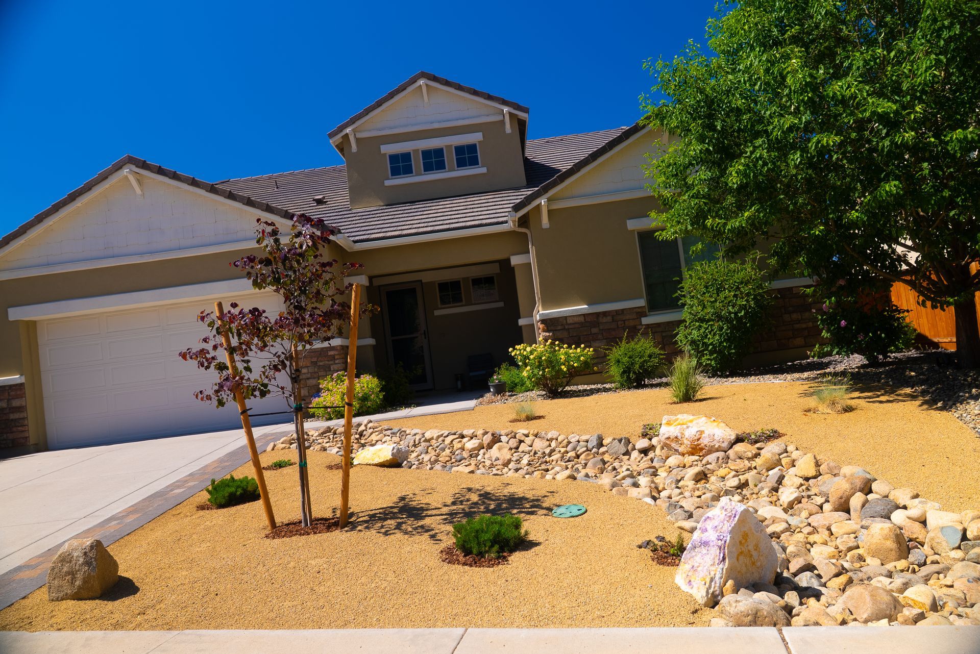 Tan house with rock landscaping under a bright blue sky.
