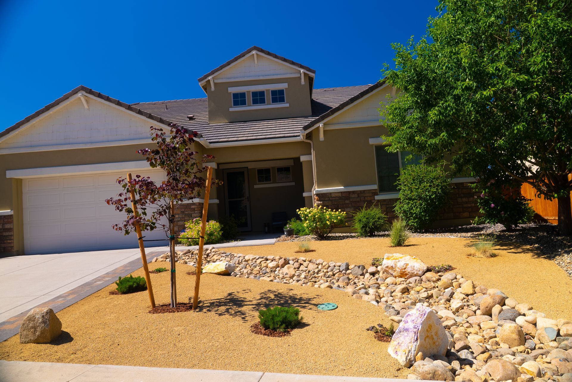 Tan house with rock landscaping, blue sky, and green tree.