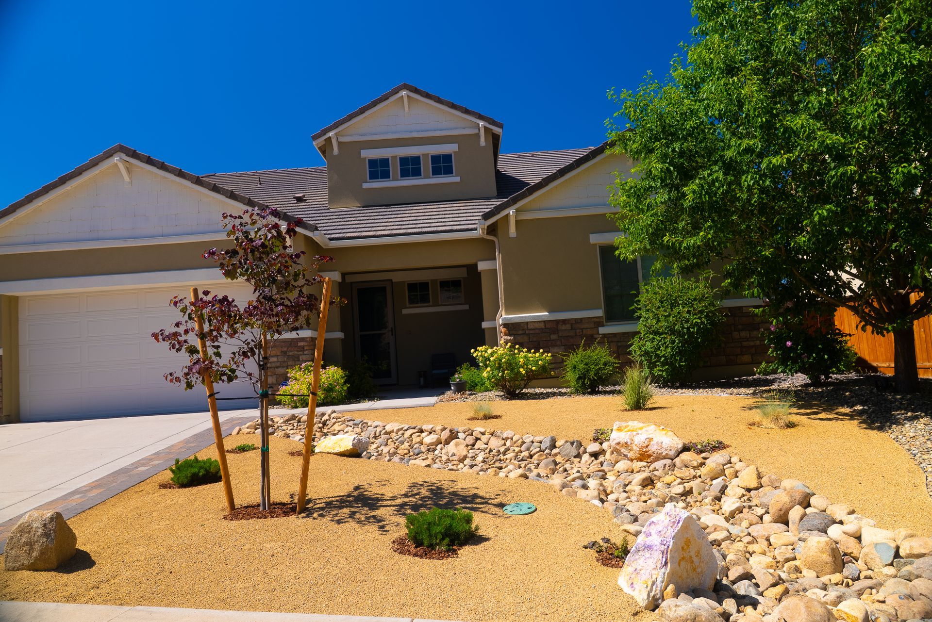 Tan house with gravel yard, rocks, and sparse landscaping under a clear blue sky.