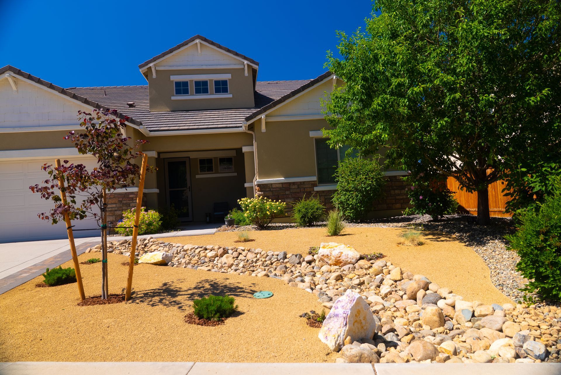 Tan house with dry creek bed landscaping, blue sky.