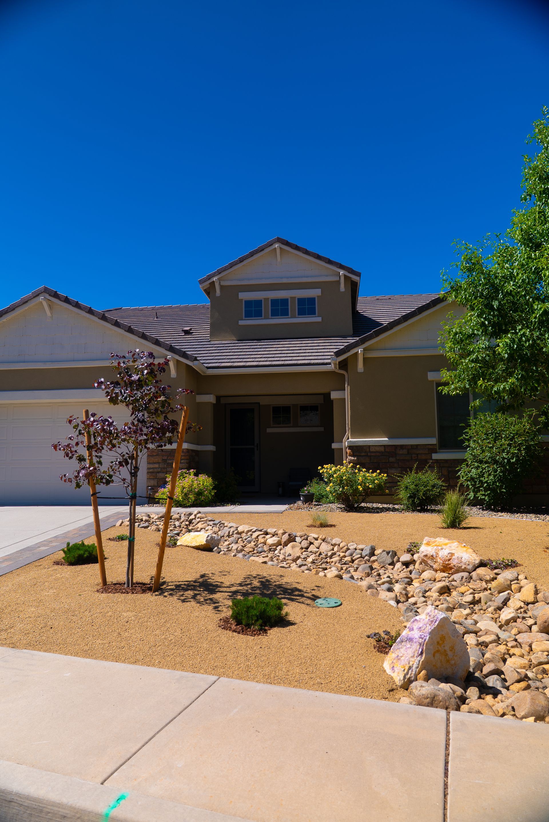 House with tan exterior, rock landscaping, blue sky.