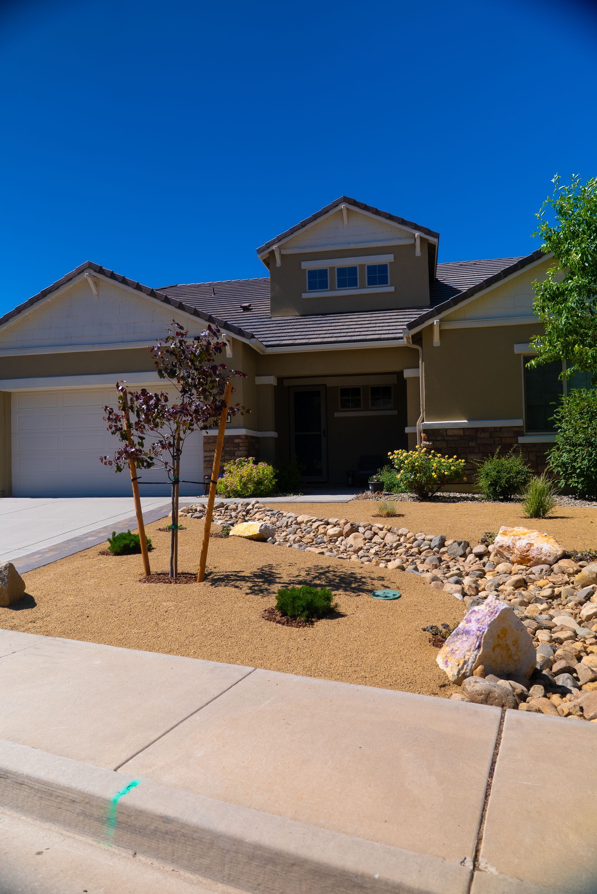 Tan house with beige roof and desert landscaping against a blue sky.