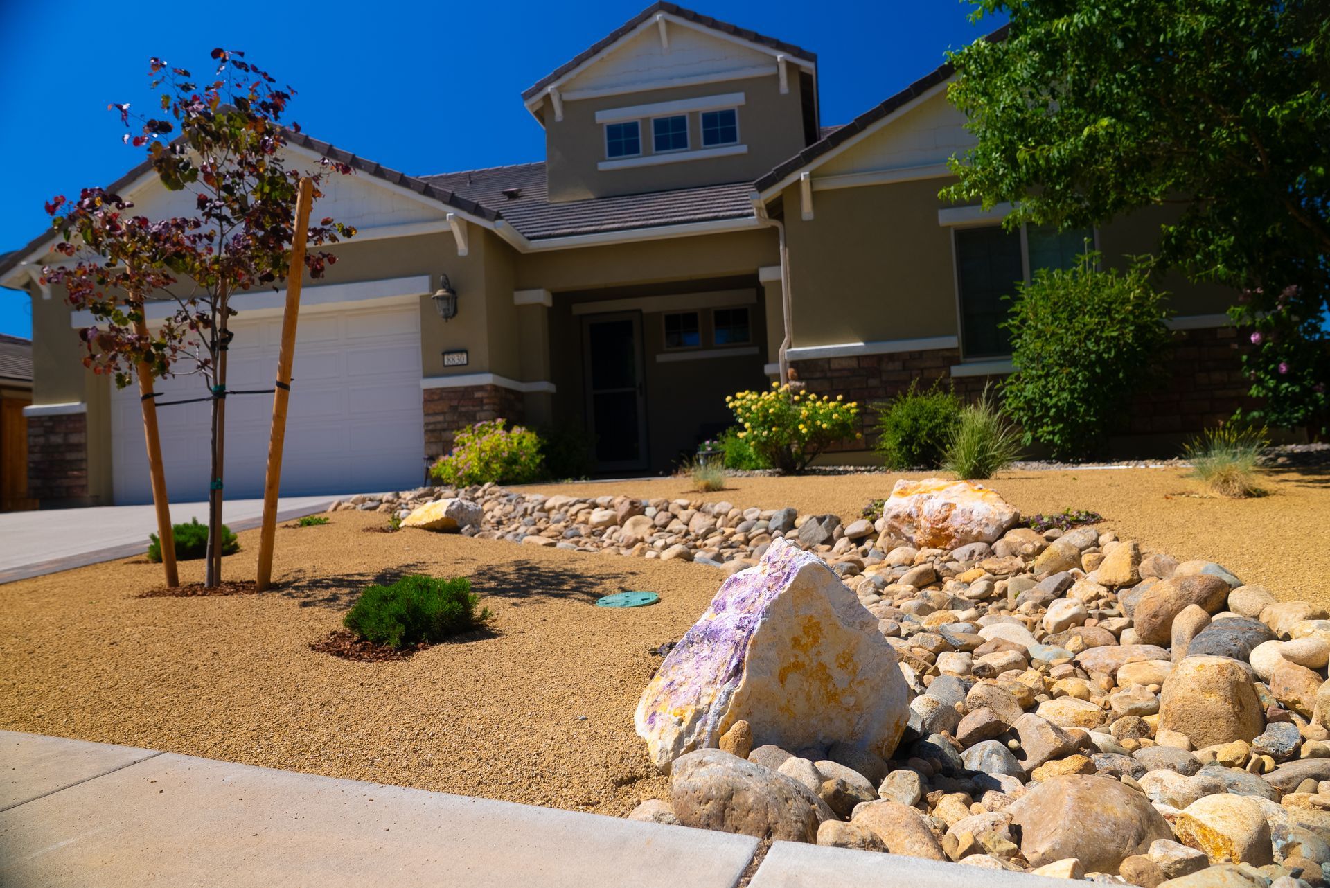 Beige house with a xeriscaped front yard, featuring gravel, rocks, and small plants.