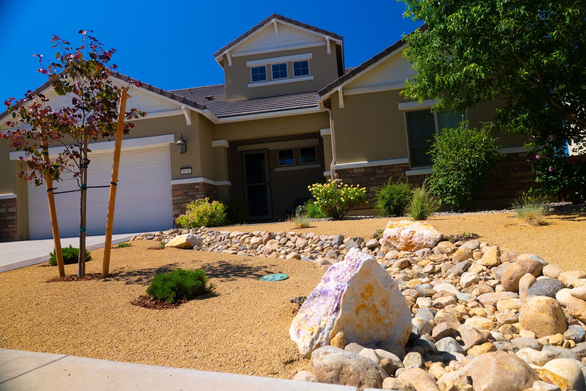Beige house with a rock-filled, xeriscaped front yard under a bright blue sky.