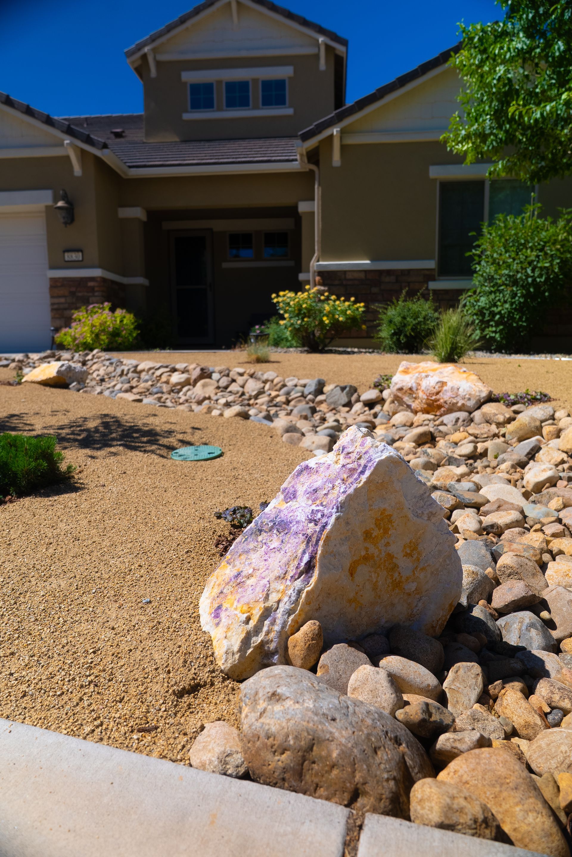 Residential home with xeriscaped front yard, featuring large rocks, gravel, and drought-tolerant plants.