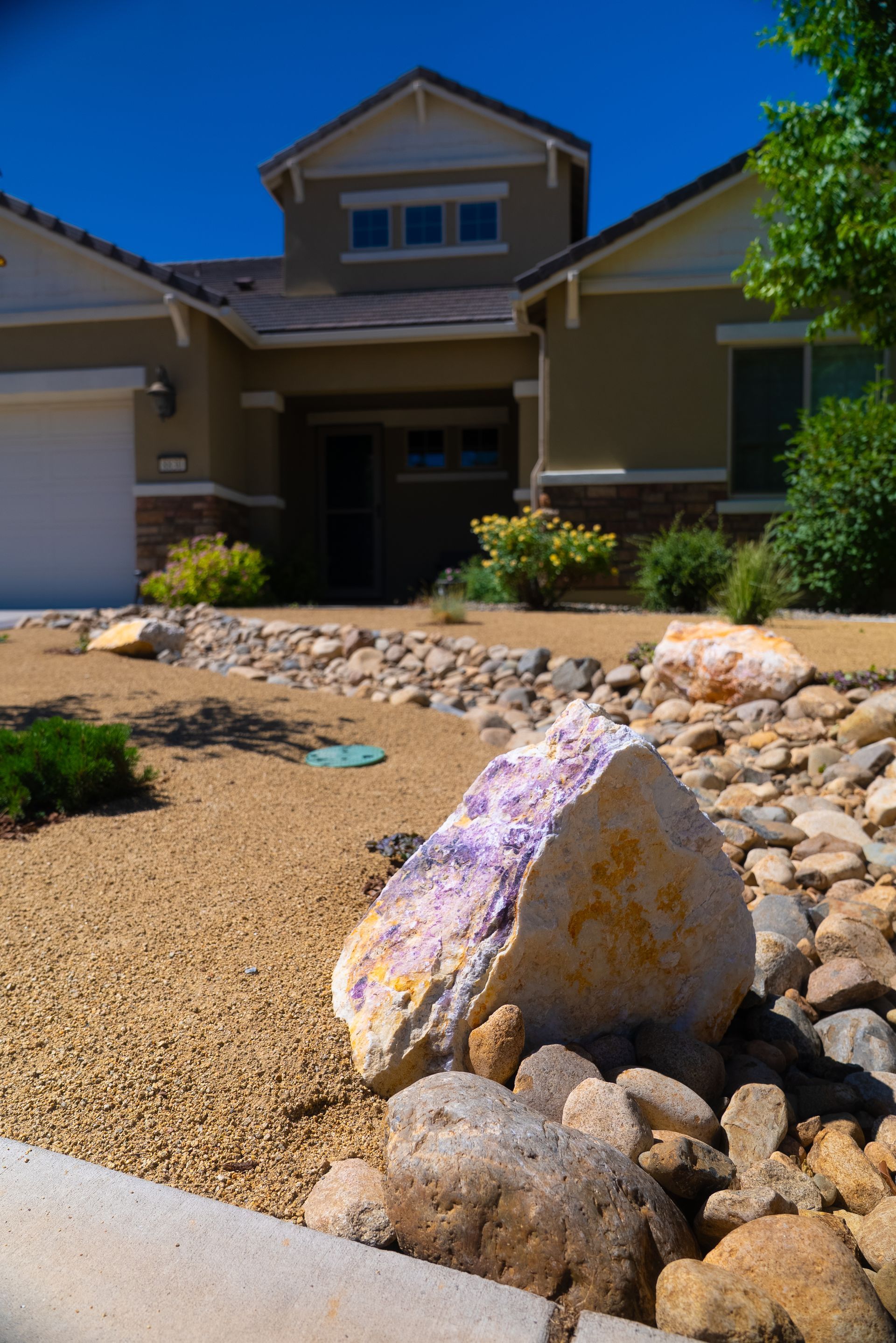 Dry landscape front yard with large, colorful rock in foreground; house in background.