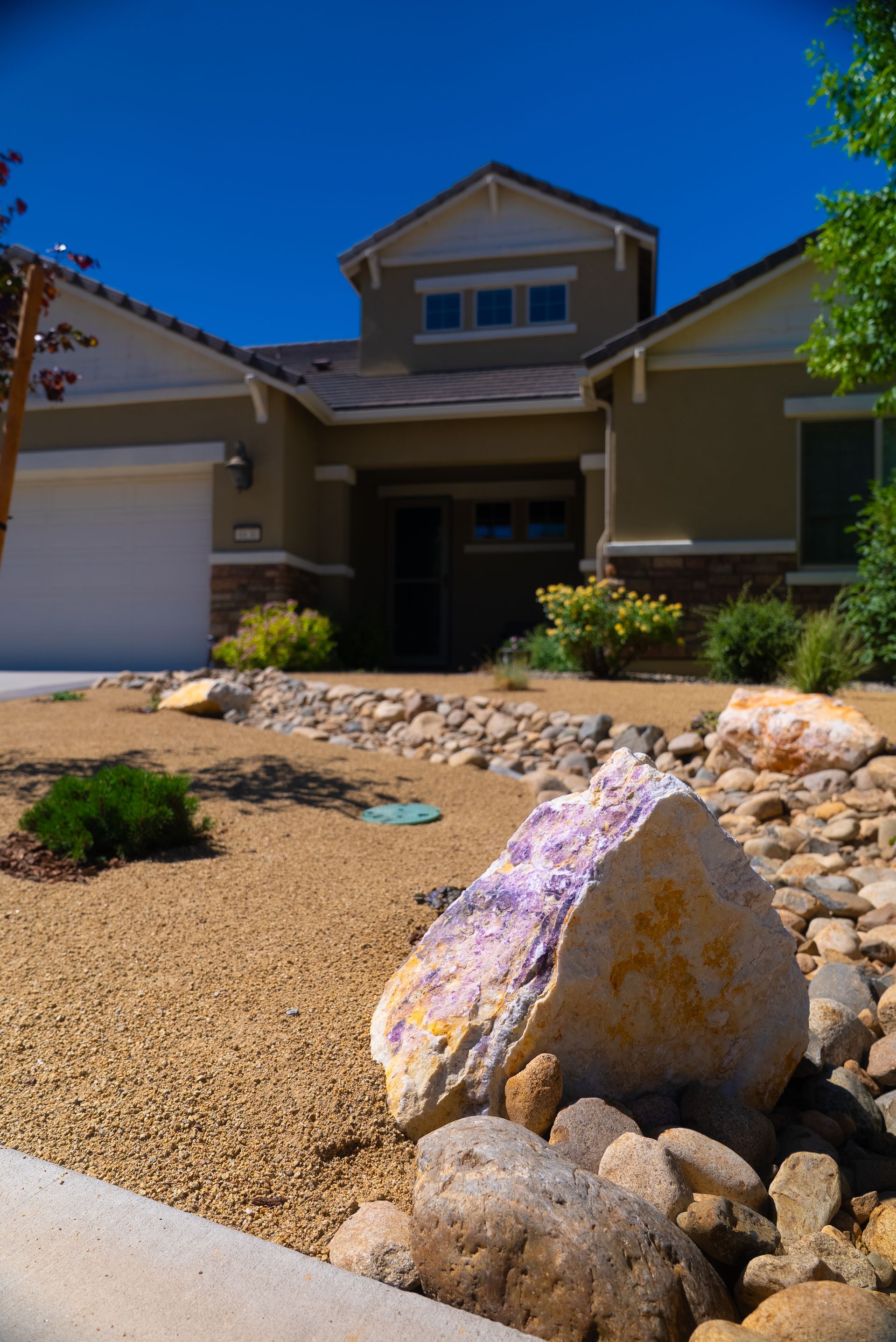 House with beige stucco and landscaping featuring rocks and desert plants on a sunny day.