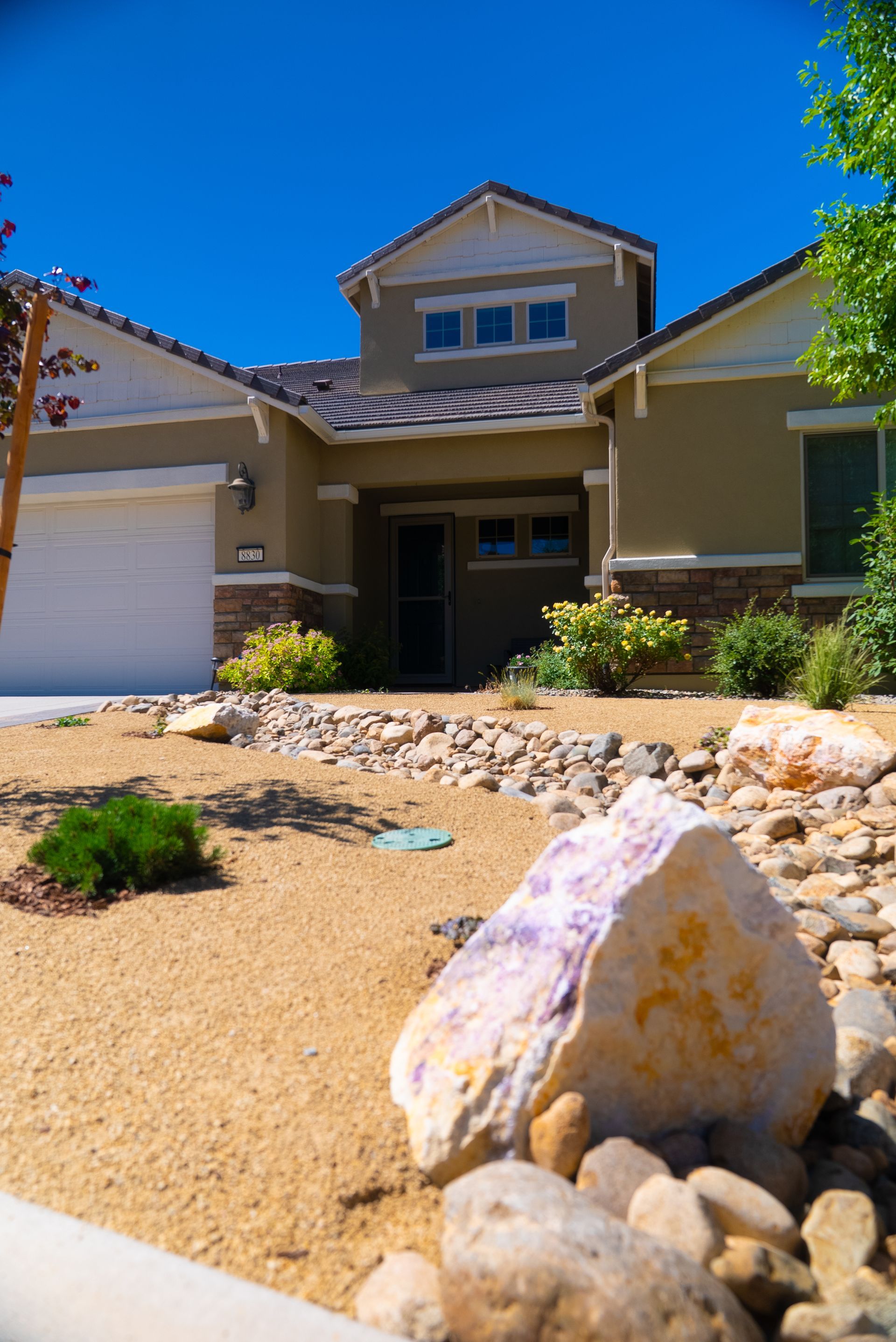 Tan and beige house with blue sky, rocks, and landscaping in front.