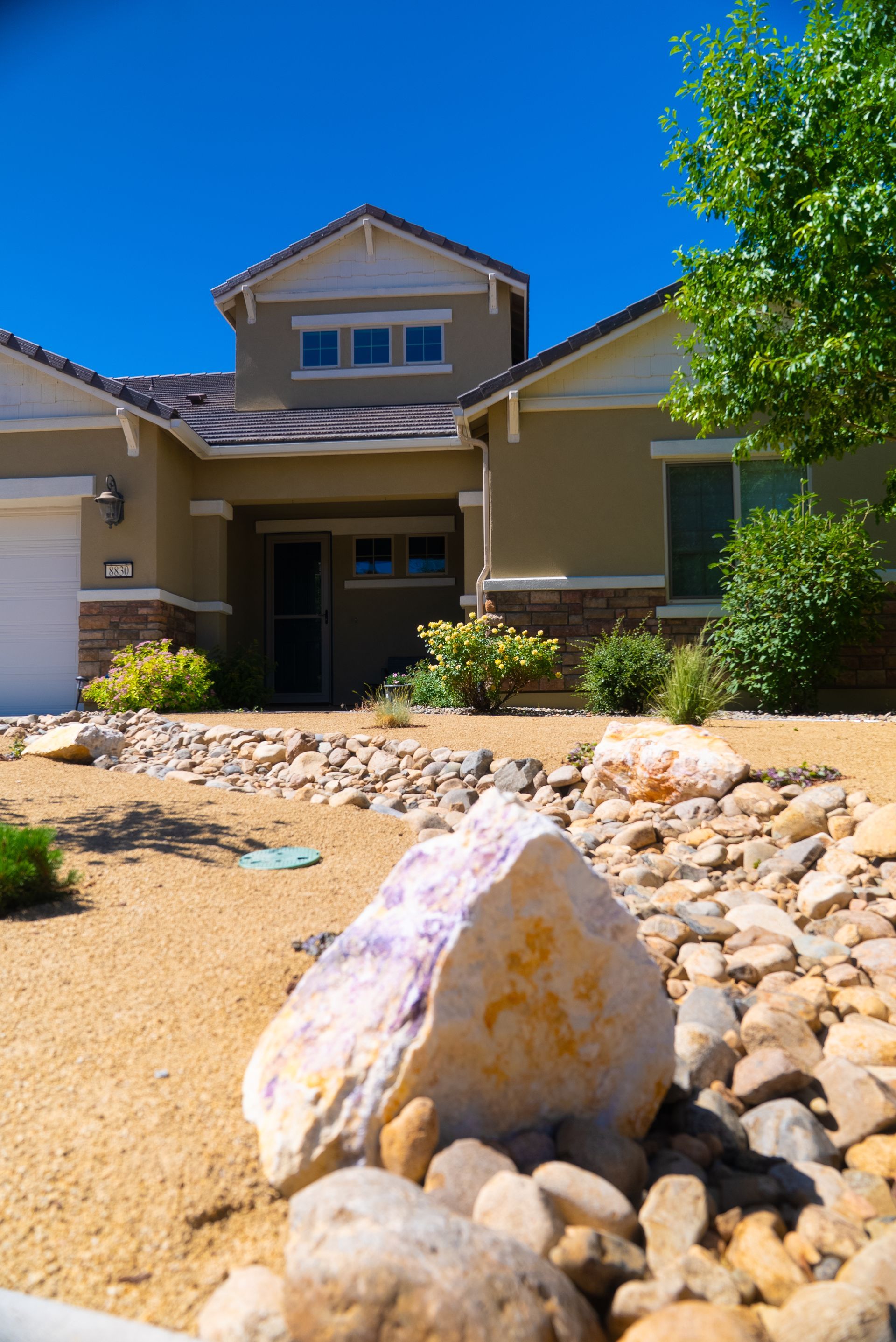 Beige house with blue sky, rocks and dry landscaping in front.