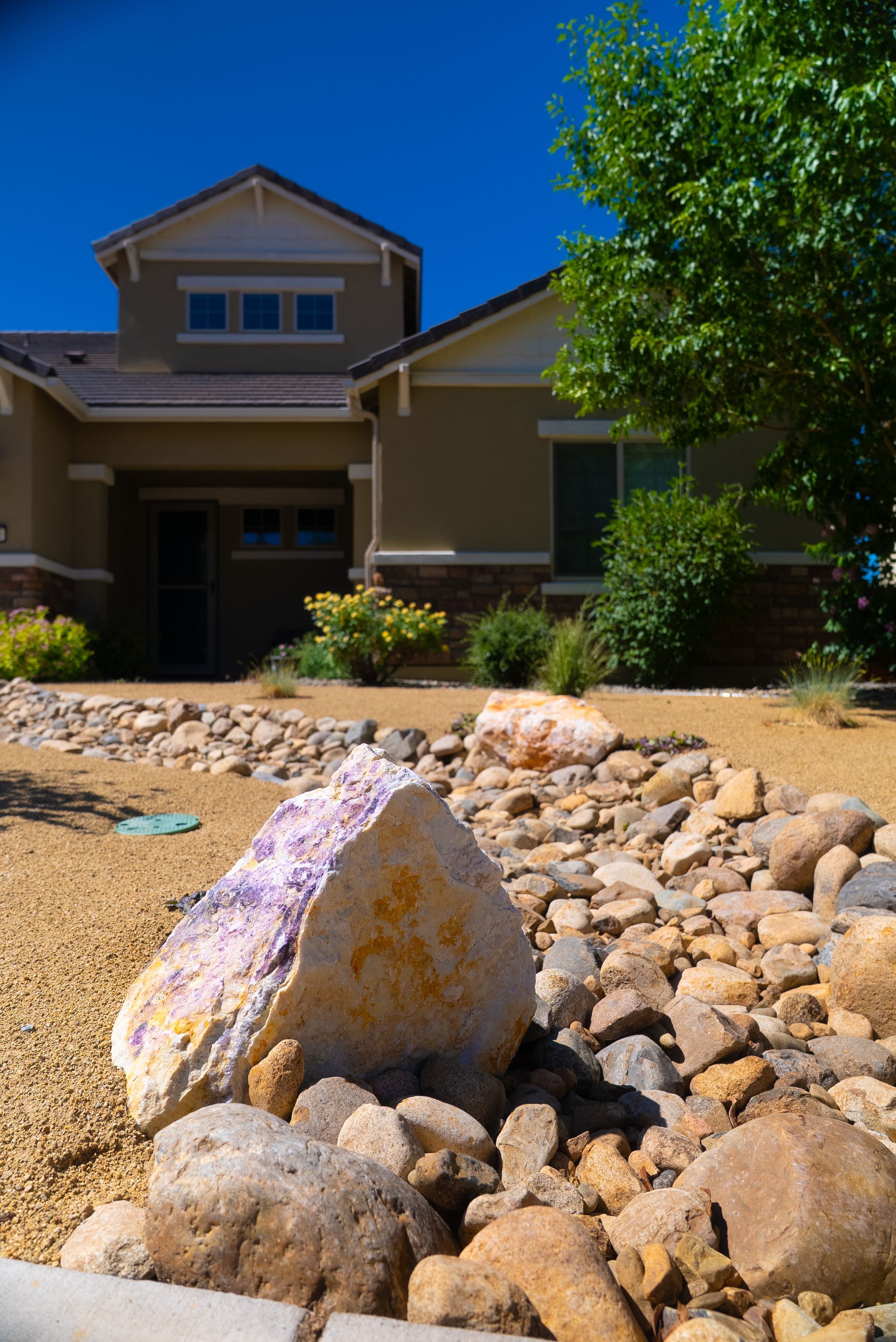 A house with a beige exterior and a rock garden in the foreground under a blue sky.