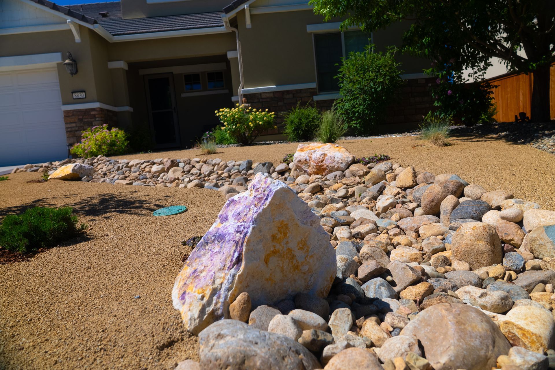 Landscaped yard with large decorative rocks and neutral-toned gravel in front of a house.