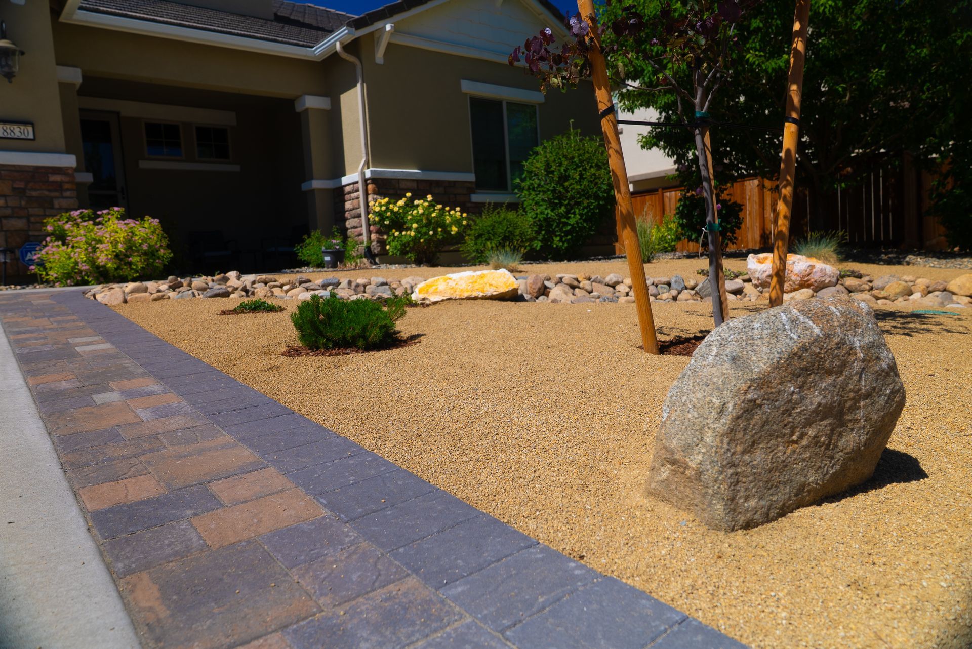 Beige house with a gravel yard, large rocks, and a brick walkway.