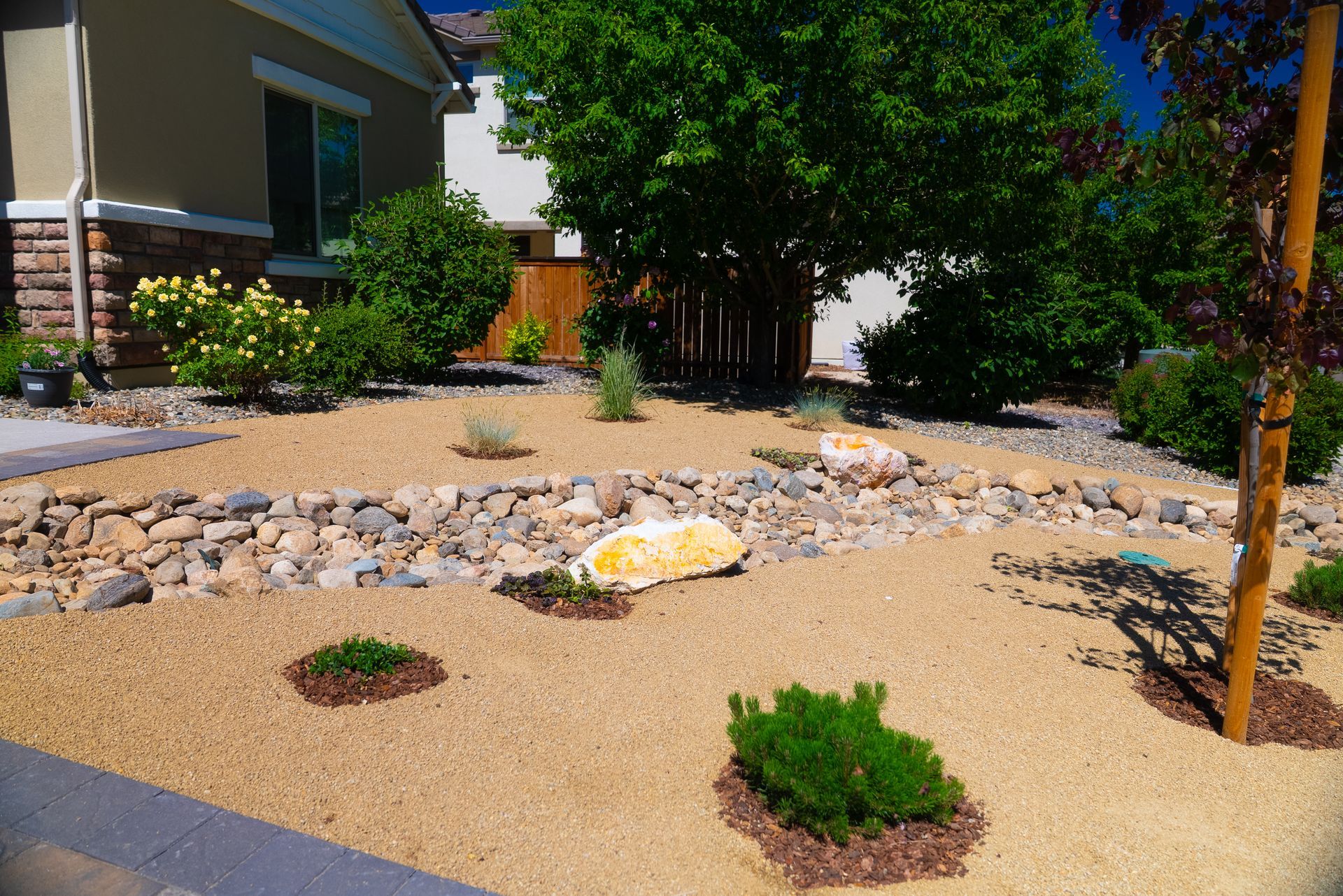 Front yard xeriscape with tan gravel, rocks, and green shrubs.