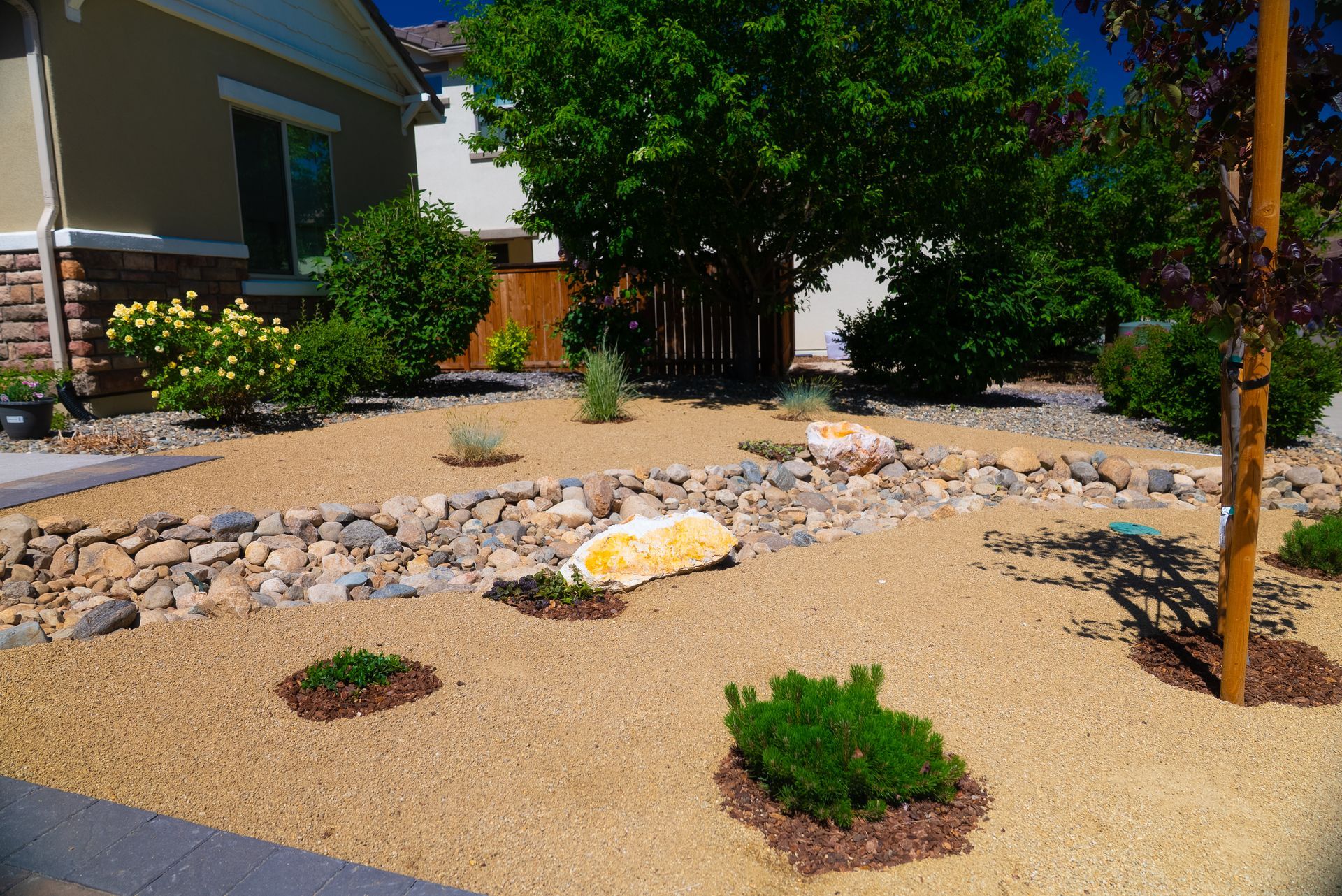 Front yard xeriscape with tan gravel, rocks, and green shrubs.