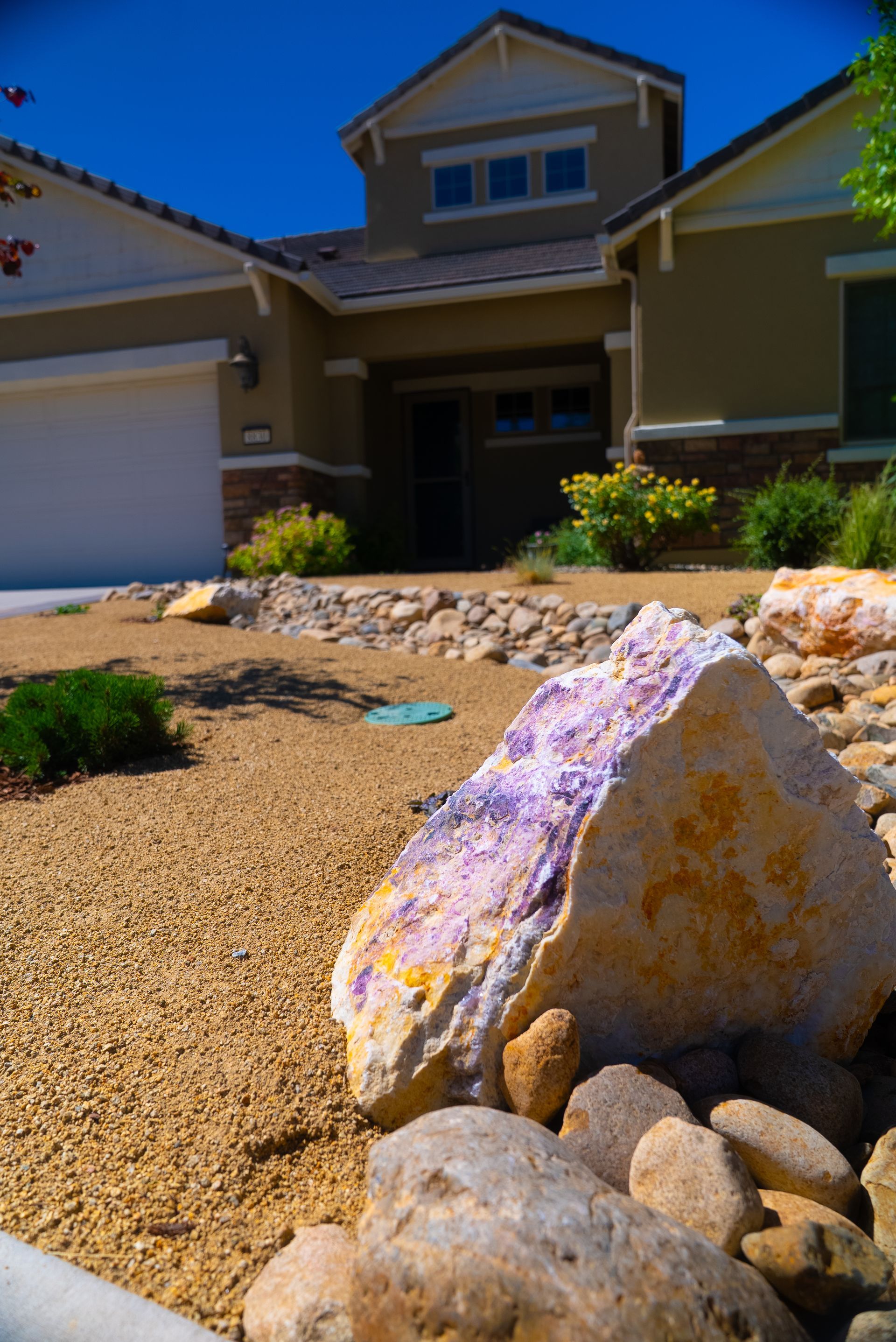 Stone landscaping in front of a tan two-story house with blue sky.