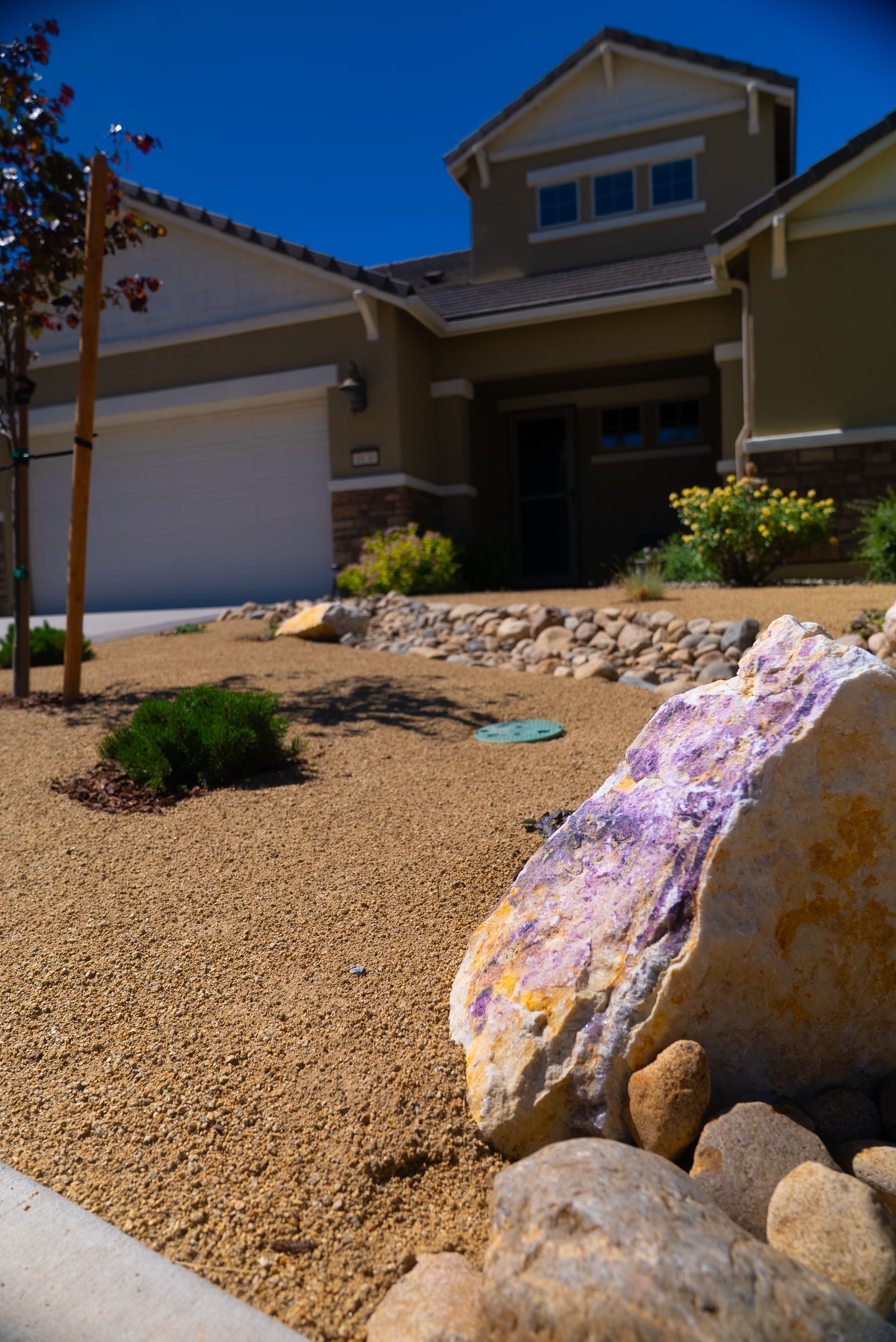 House with xeriscaped front yard, including tan gravel, large rocks with purple accents, and sparse plants.
