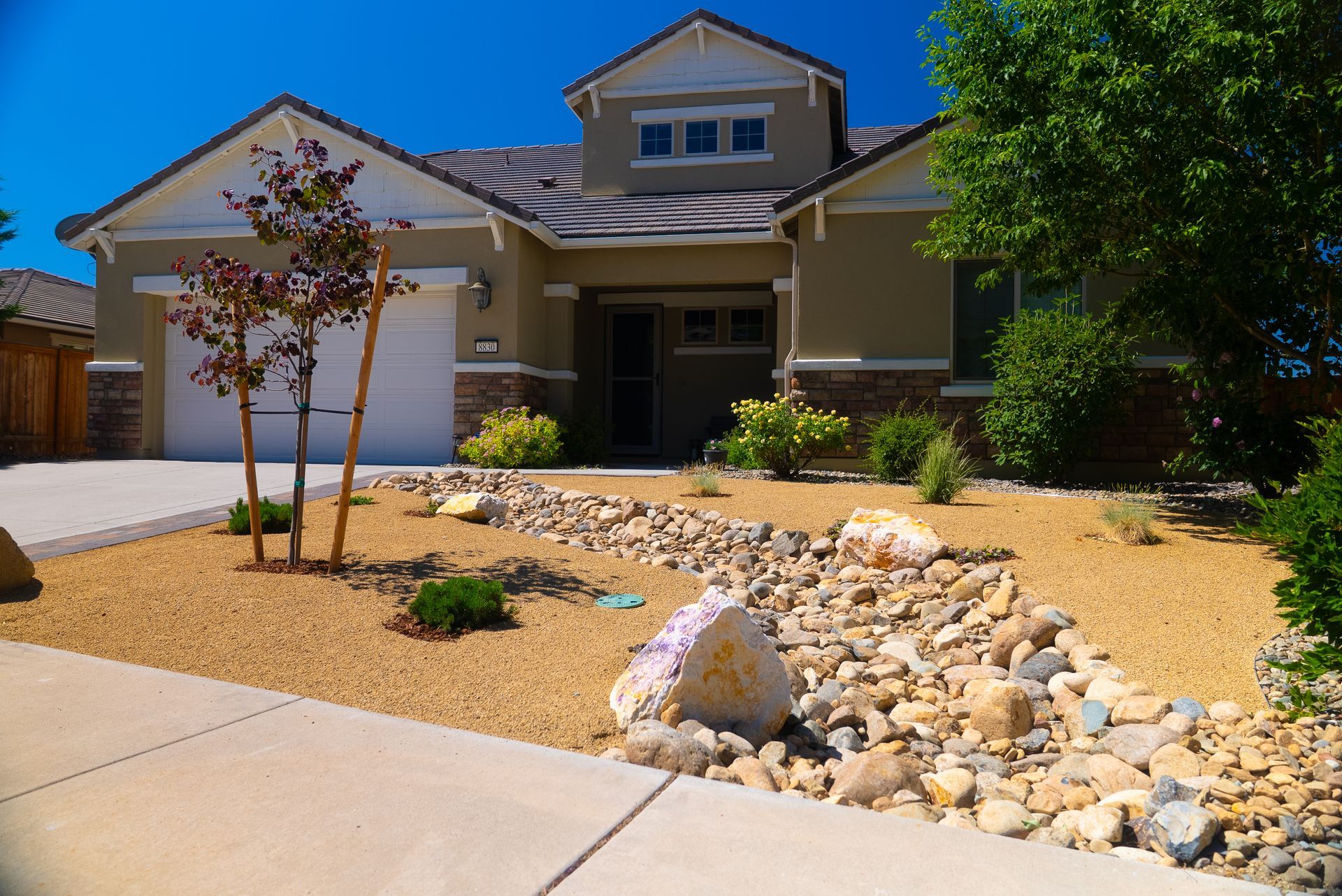 Beige house with landscaping, a dry creek bed, and tan mulch.