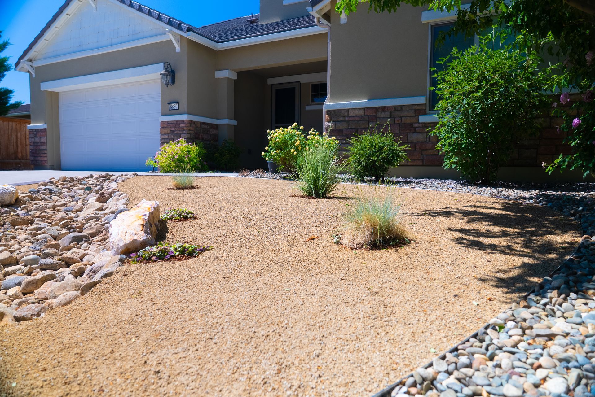 Front yard with drought-tolerant landscaping: gravel, rocks, and small plants in front of a beige house with a garage.