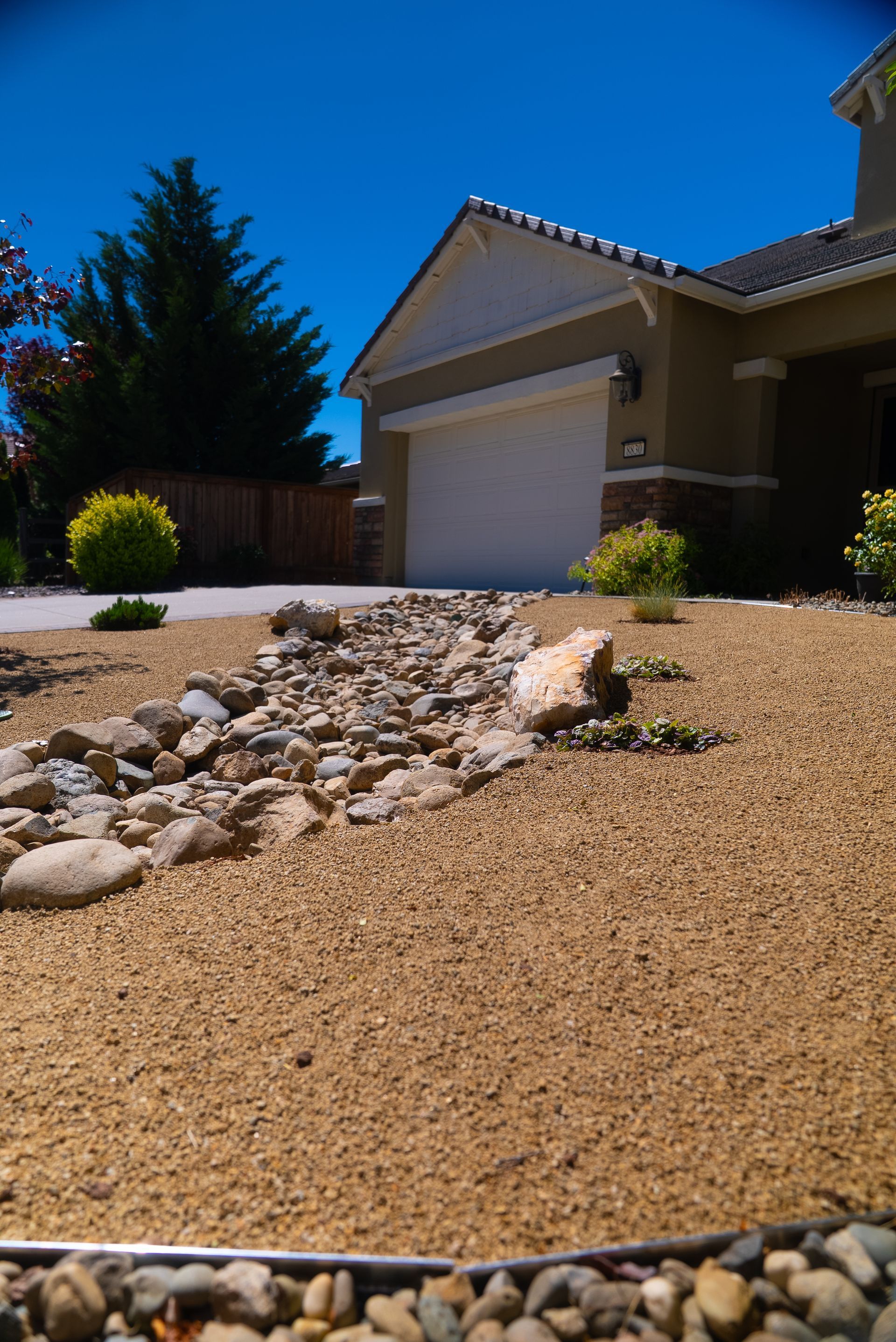 Dry creek bed landscaping in front of a tan house with blue sky.