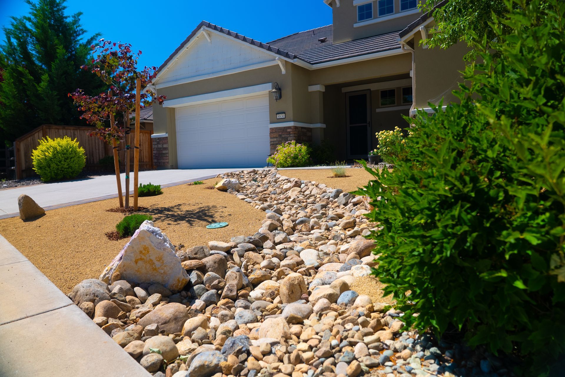 Front yard xeriscape with a house in the background, featuring a dry creek bed and drought-tolerant landscaping.