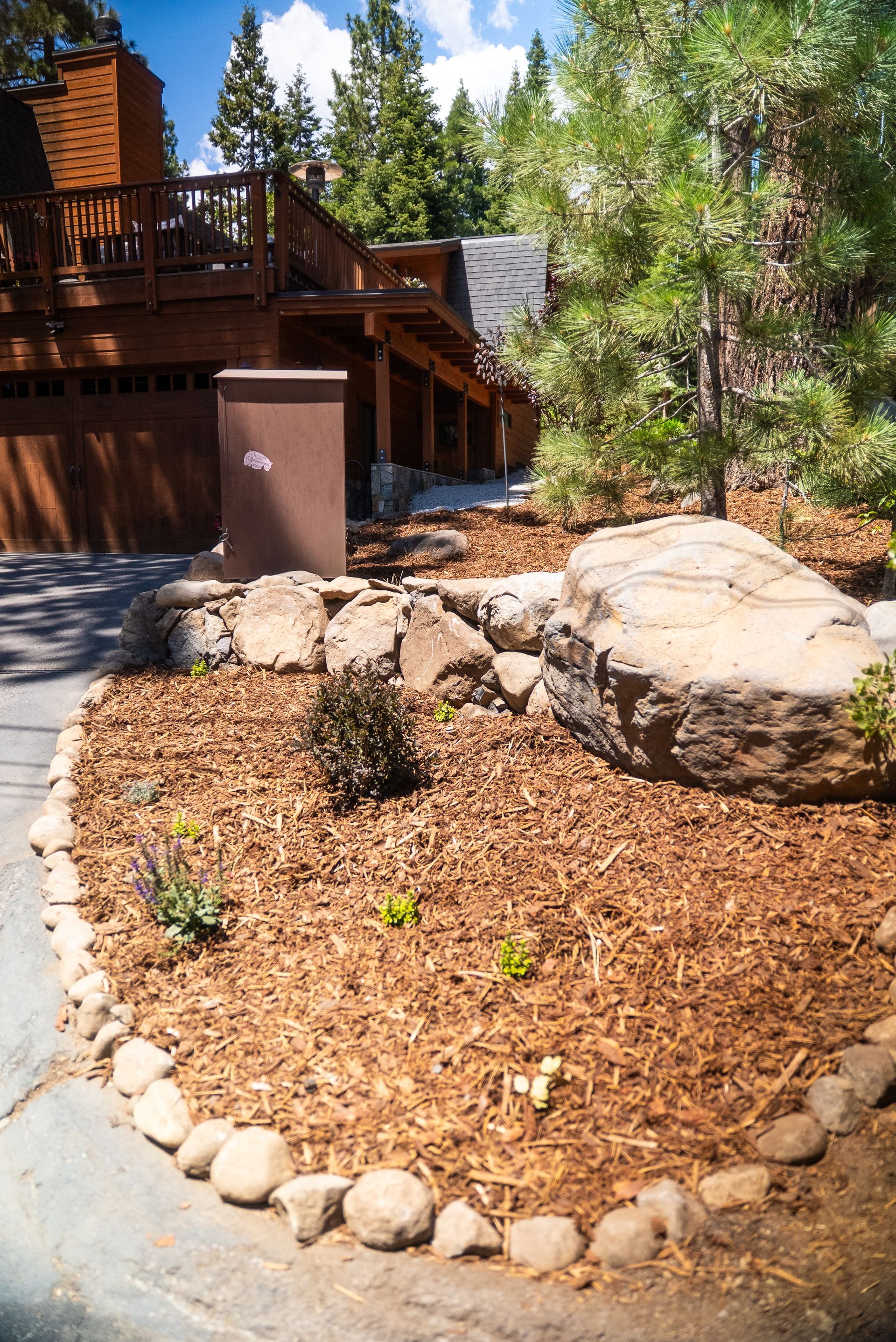 Brown wooden house with rock garden, brown mulch, and large boulder.