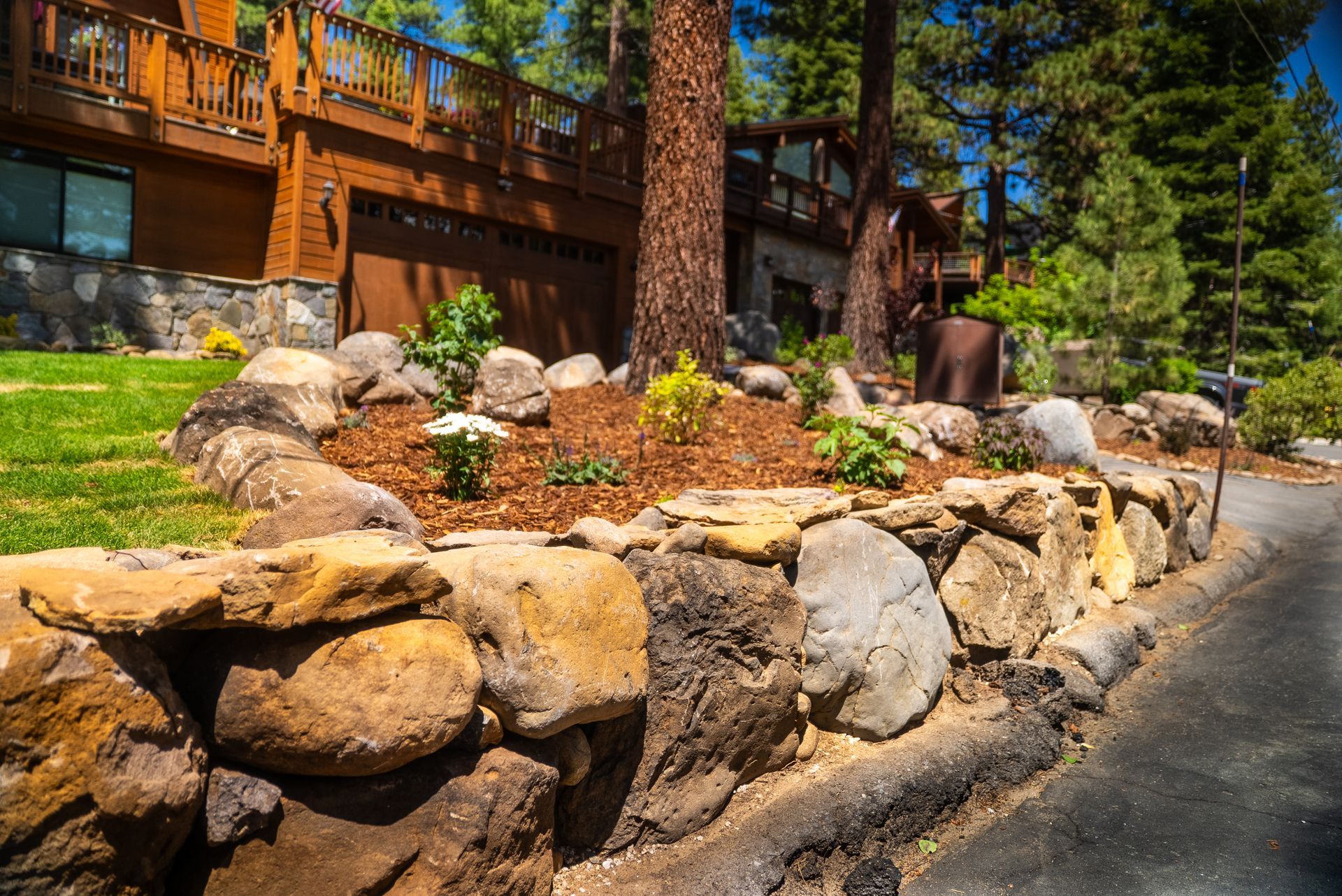 Stone retaining wall with a landscaped area in front of a wood-sided house.