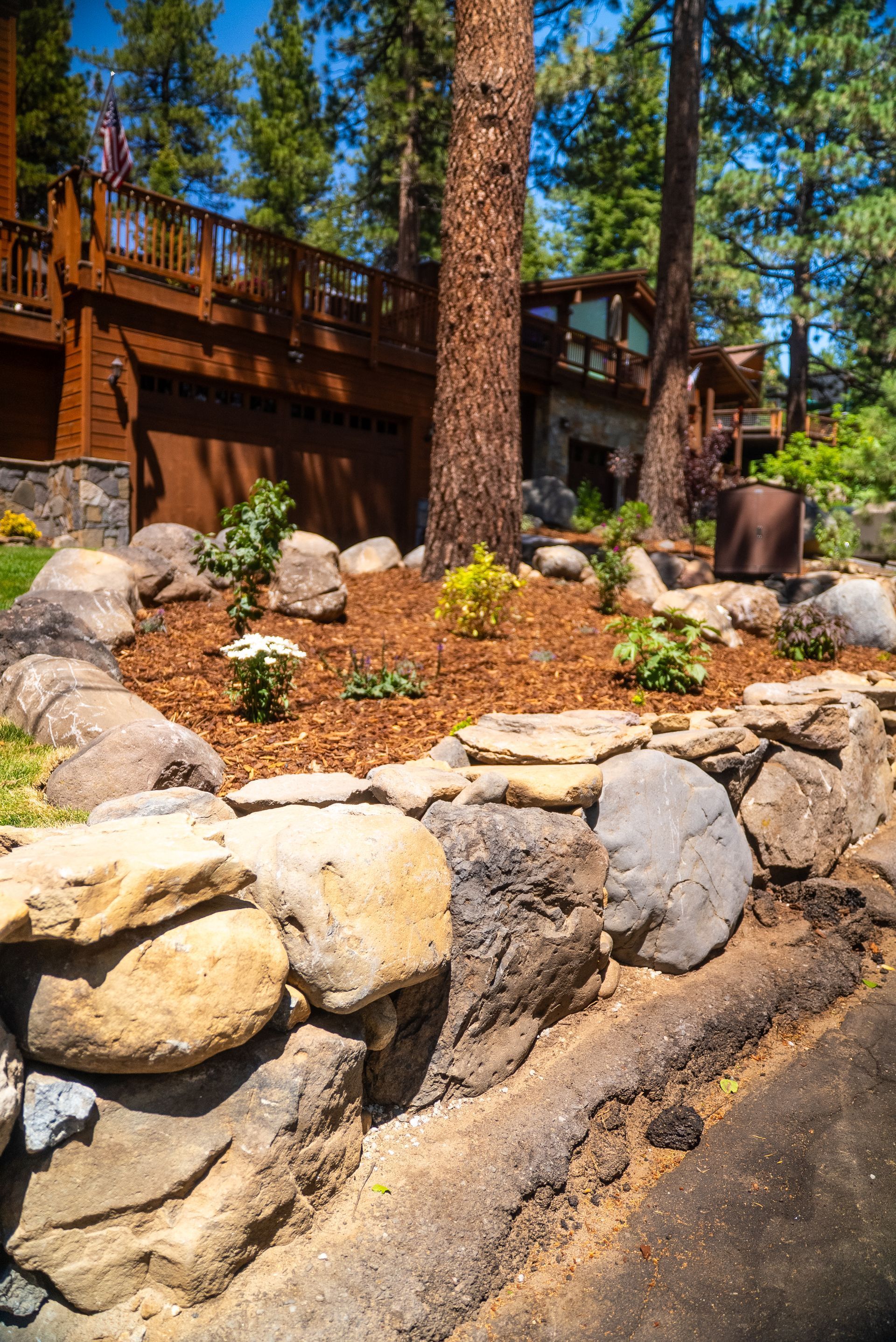 Stone retaining wall with a landscaped area in front of a wood-sided house.
