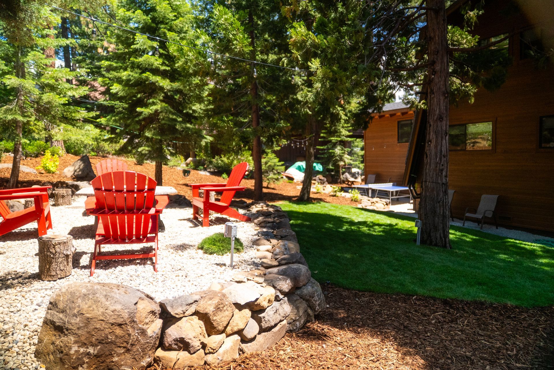 Red Adirondack chairs on a gravel patio with trees and a wooden building in the background.
