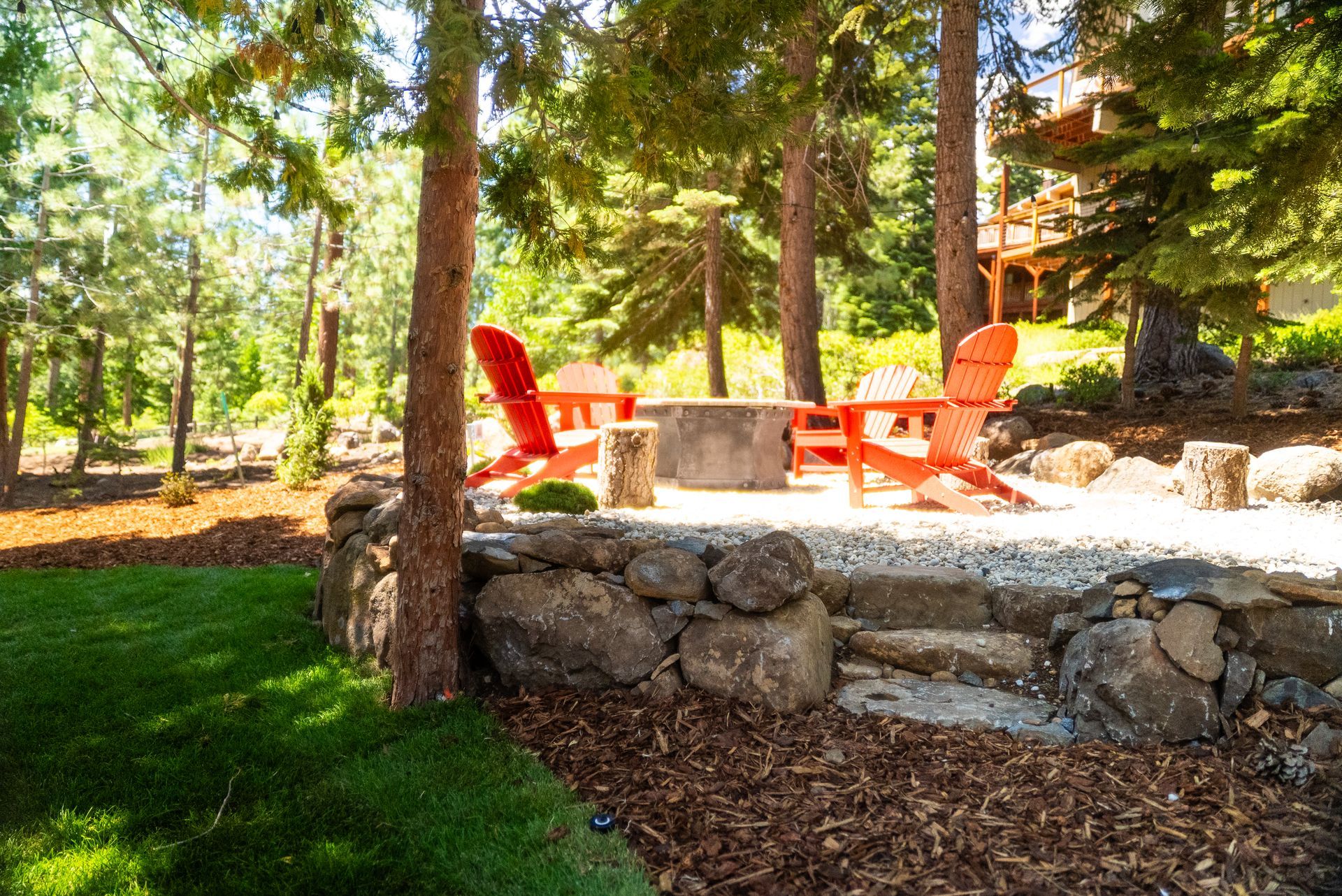 Outdoor patio with two orange Adirondack chairs around a fire pit, surrounded by trees.