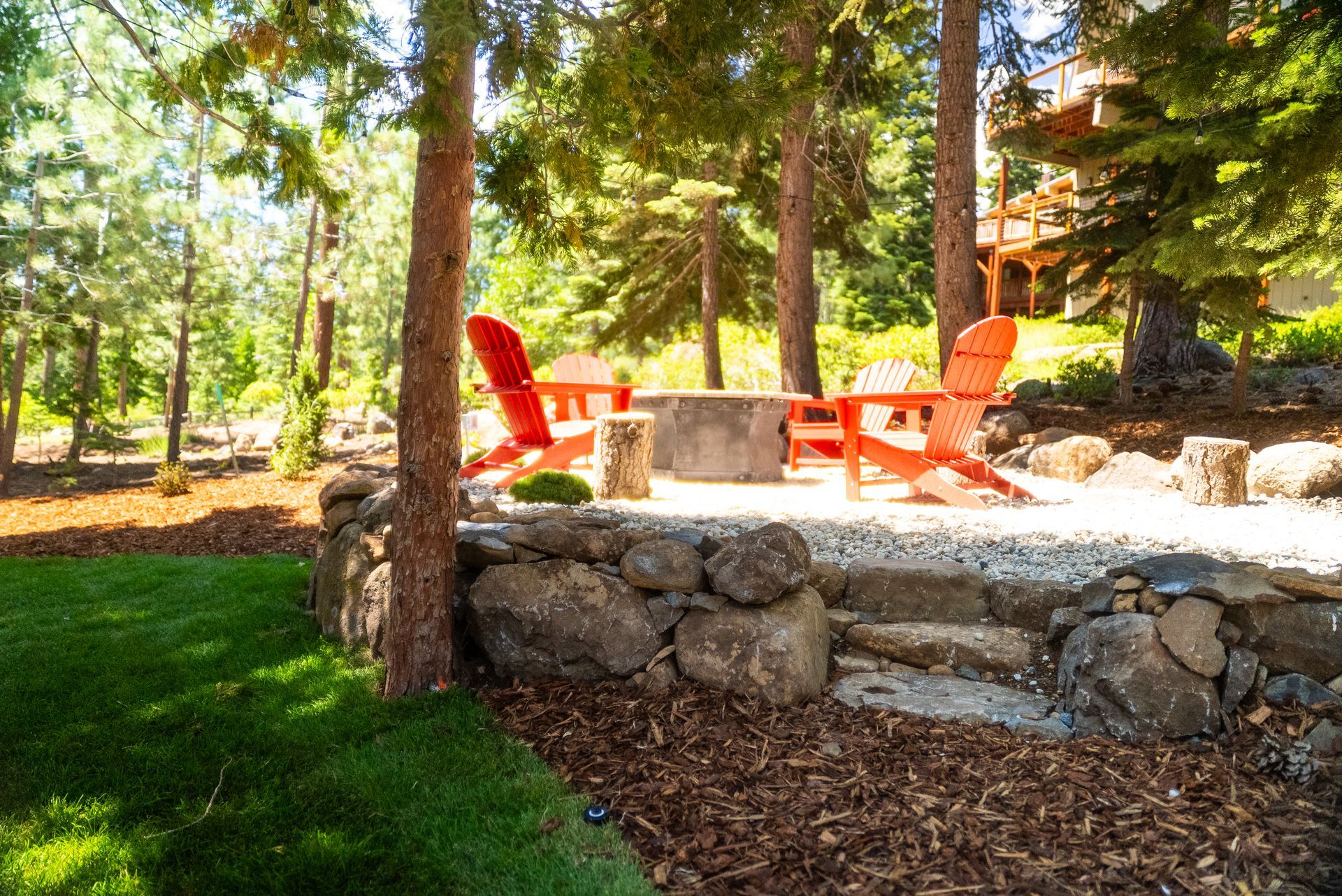 Two orange Adirondack chairs around a fire pit in a wooded backyard setting.