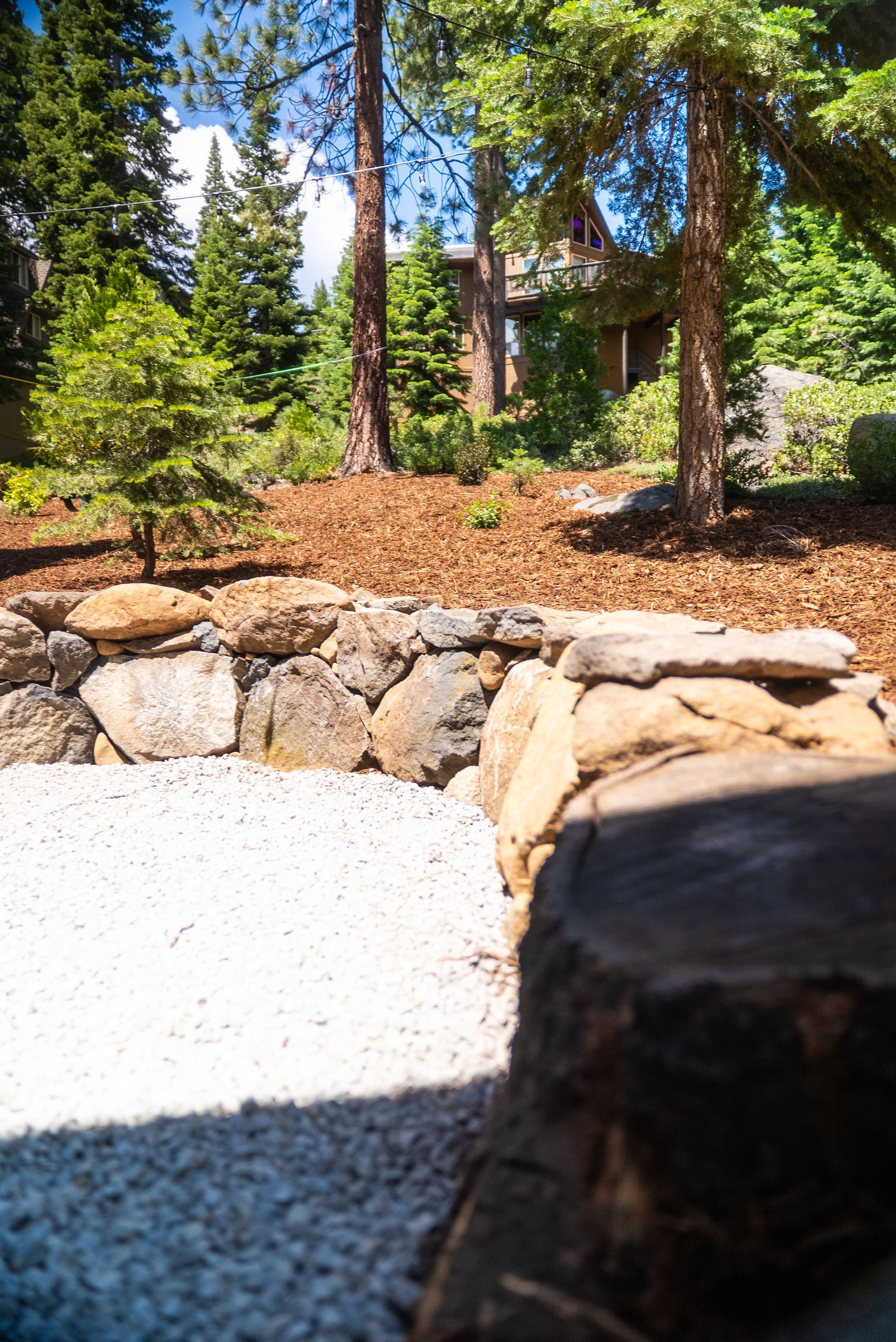 Stone wall and gravel area with a view of trees and a building in the background.