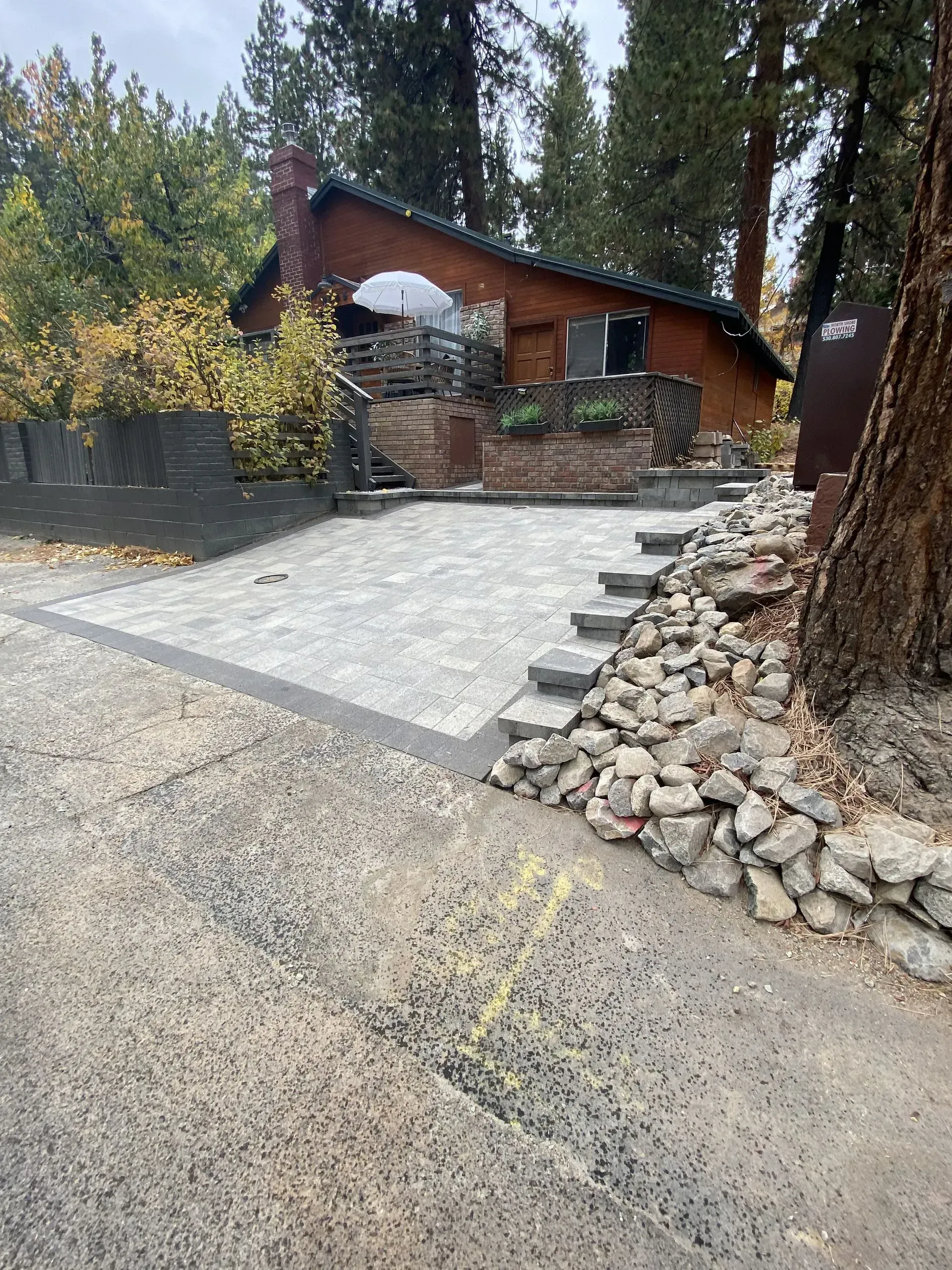 Cabin with paved driveway and stairs; surrounded by rocks and trees.