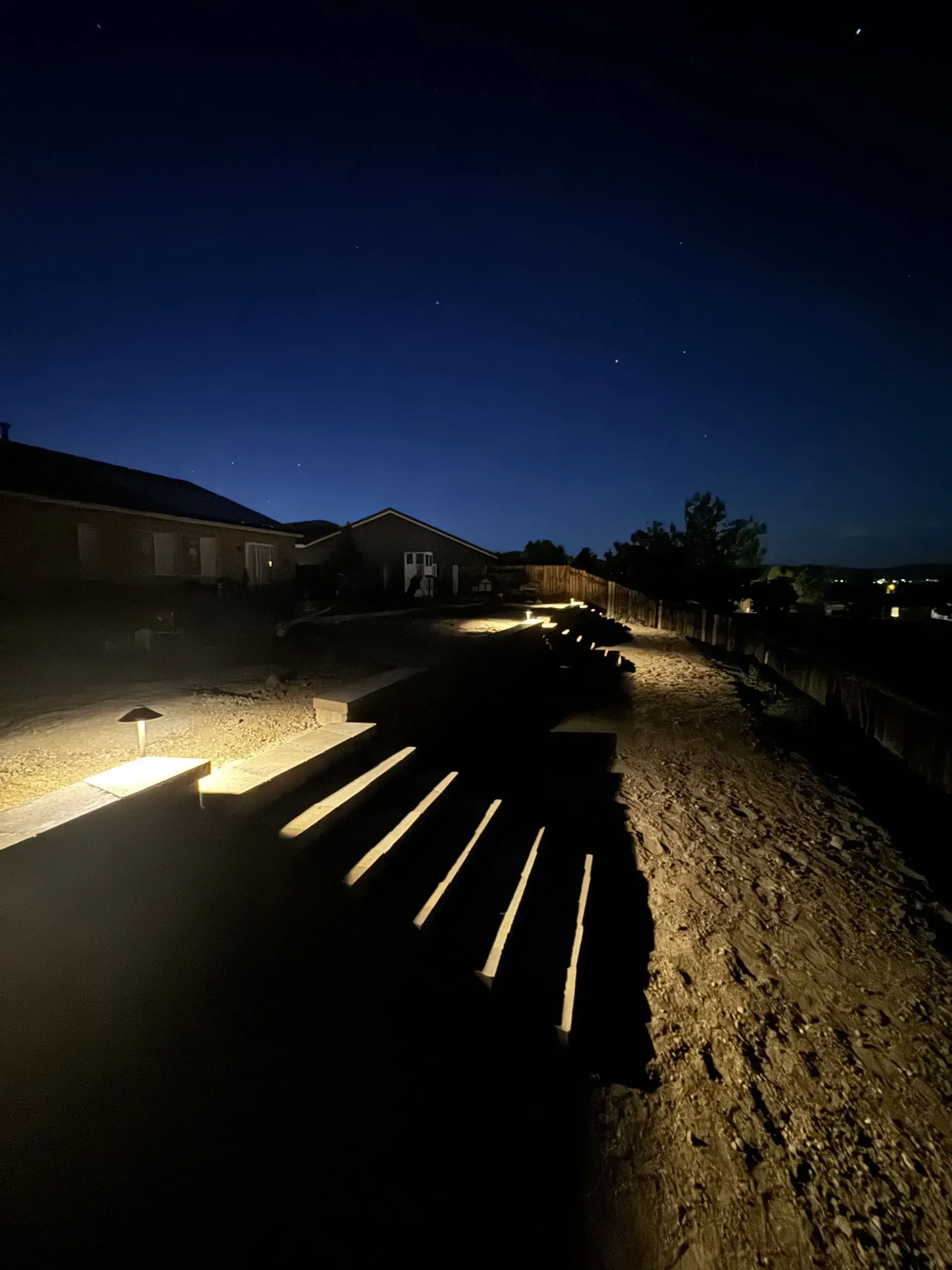 Path lit by spotlights leads towards a house at night.
