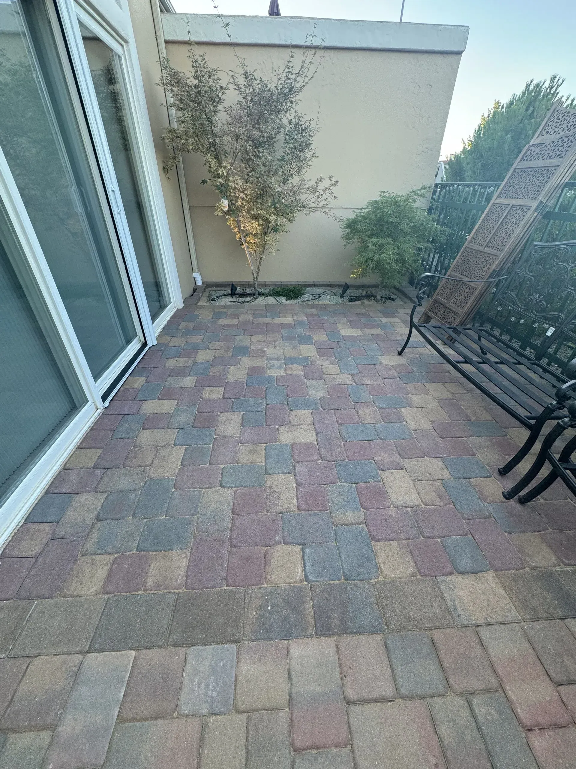 Brick patio with multi-colored bricks, a bench, and a tree. Sliding glass door on the left.