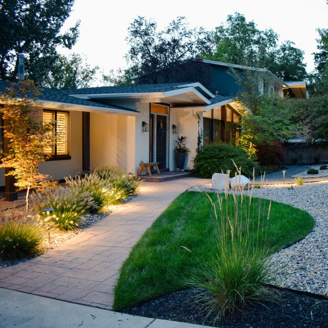 Brick pathway leading to a home's front door, with steps, landscaping, and a blue window.