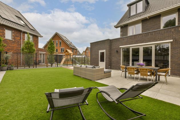 Backyard with patio, lawn, seating, and houses in background.