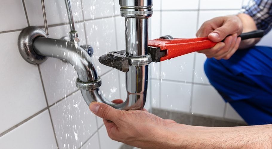 Plumber Using a Wrench on a Leaky Chrome Pipe Under a Sink — Expert Plumbing & Solar Services Bathurst in Kelso, NSW