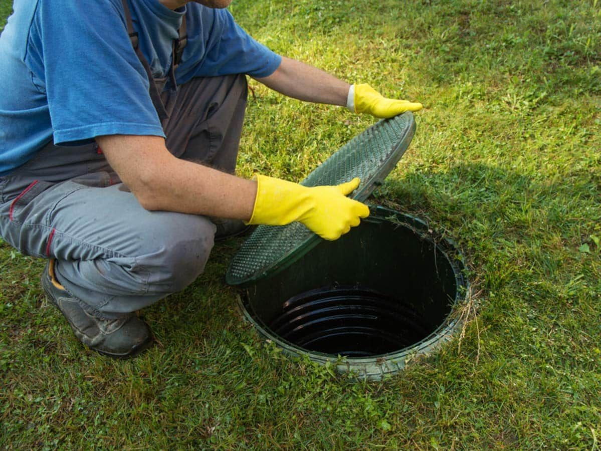 Person in Blue Overalls and Yellow Gloves Opening Septic Tank Lid in Grassy Yard — Expert Plumbing & Solar Services Bathurst in Kelso, NSW