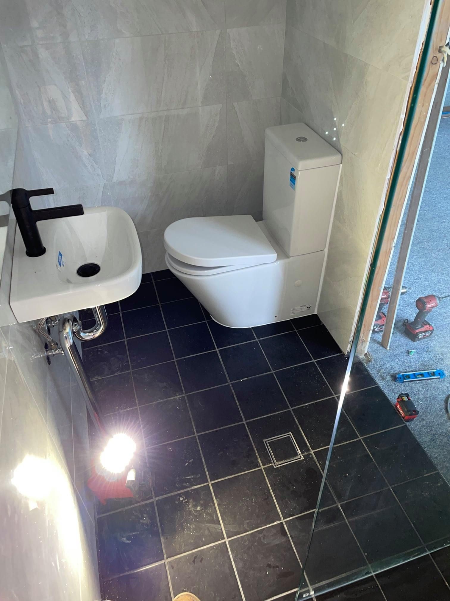 Small Bathroom With Black Floor Tiles, White Walls — Expert Plumbing & Solar Services Bathurst in Kelso, NSW