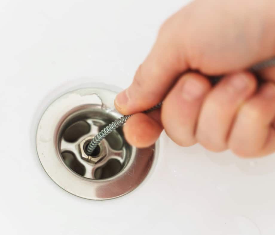 Hand Using a Drain Snake to Clear a Clogged Sink Drain — Expert Plumbing & Solar Services Bathurst in Lithgow, NSW