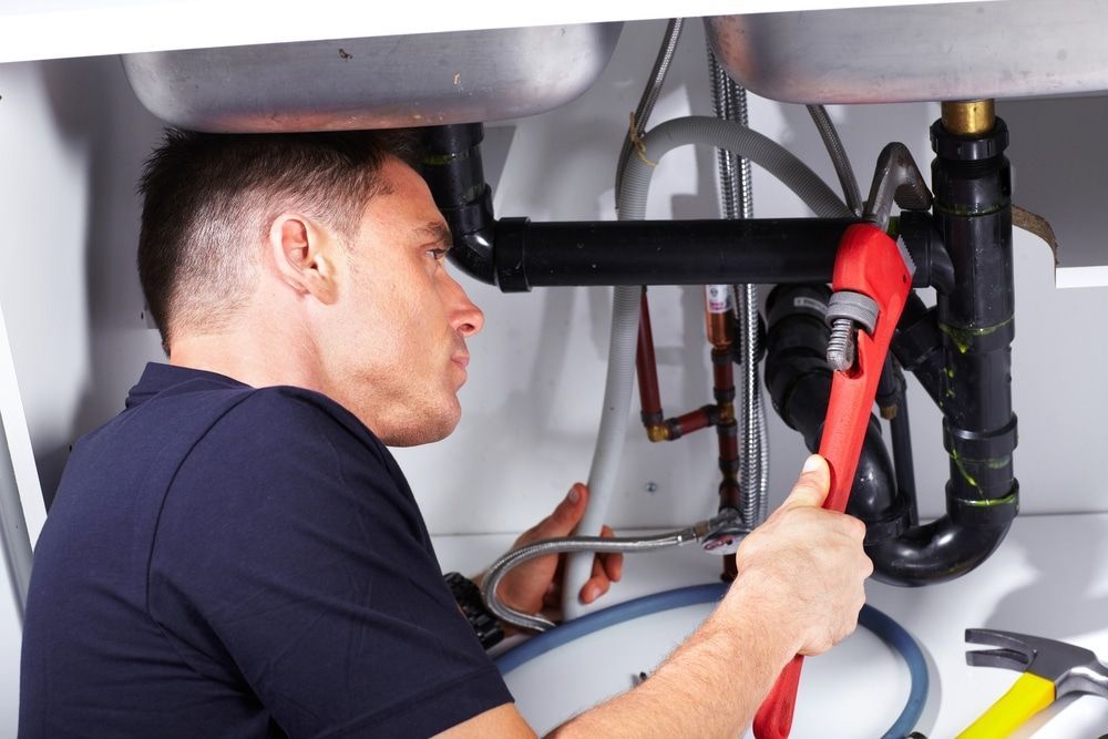 Plumber Under a Sink, Using a Wrench — Expert Plumbing & Solar Services Bathurst in Lithgow, NSW