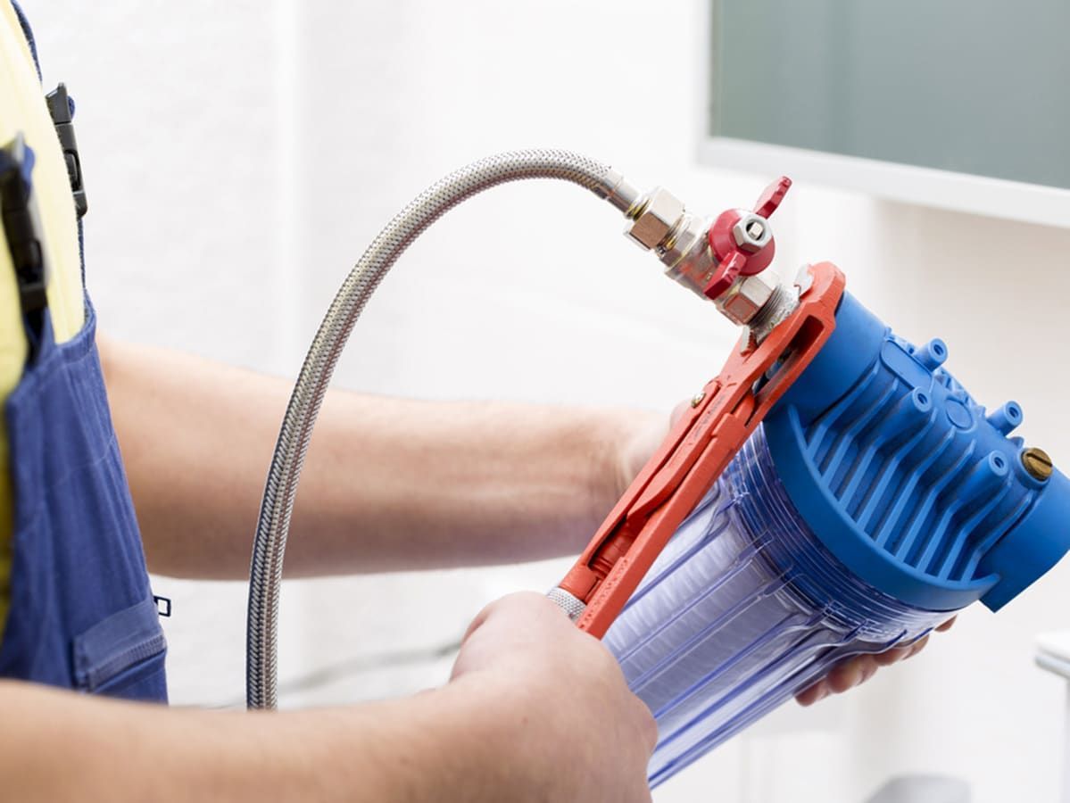 Person Installing a Water Filter, Holding the Unit With a Hose Attached — Expert Plumbing & Solar Services Bathurst in Lithgow, NSW