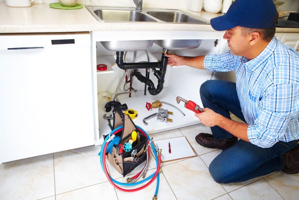 Plumber Kneeling Under a Kitchen Sink — Expert Plumbing & Solar Services Bathurst in Lithgow, NSW