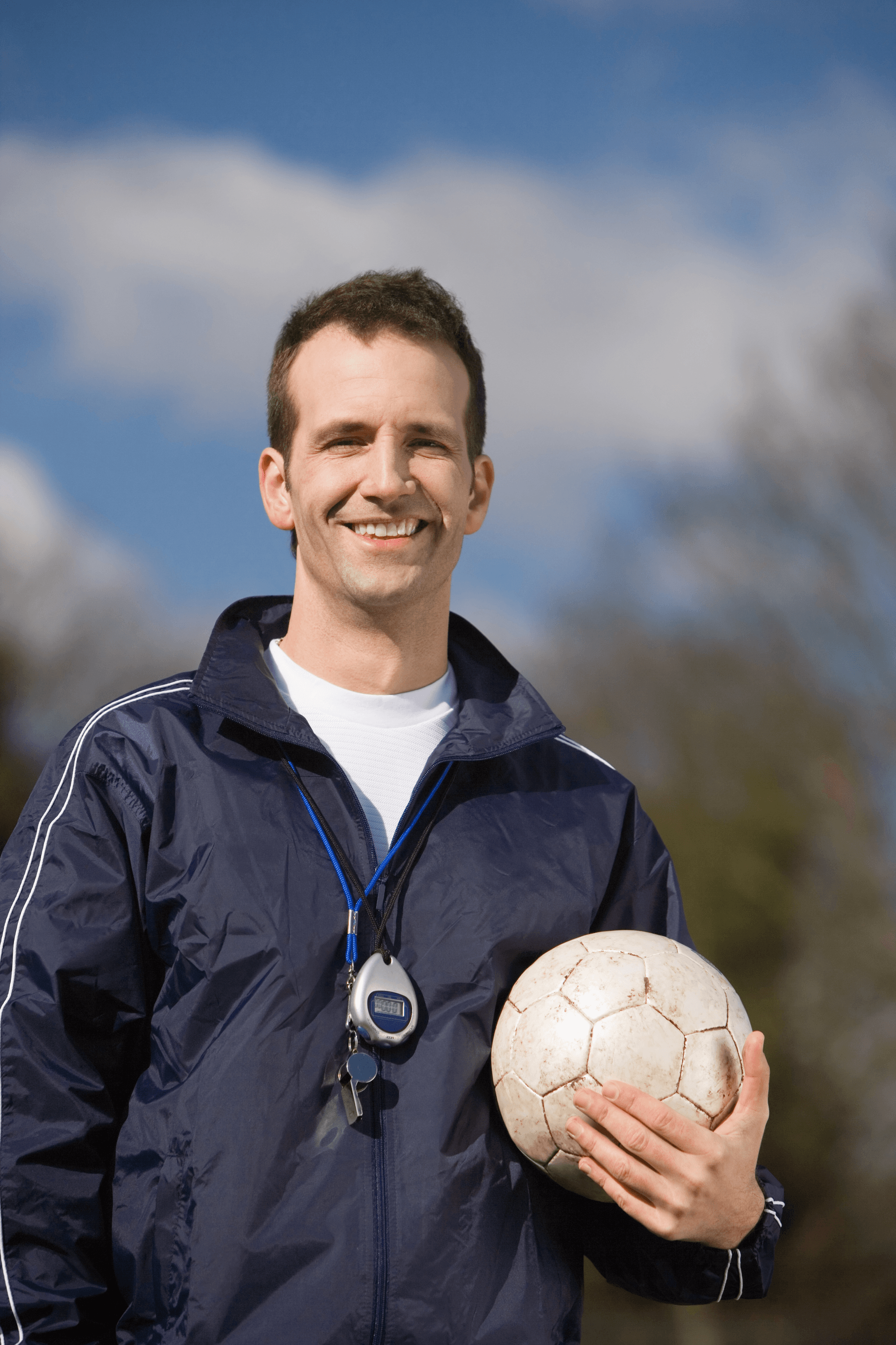 Person in a navy jacket holding a white soccer ball outdoors against a blue sky.