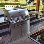 Stainless steel outdoor gas grill built into a stone patio counter with side burner.