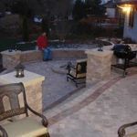 Patio at dusk with stone planters, benches, and a person in a red jacket near the center